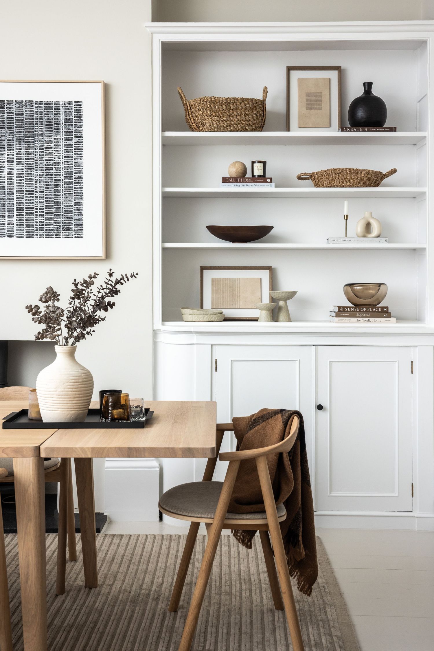 Modern white built-in shelving unit with wooden dining table and neutral decor elements.