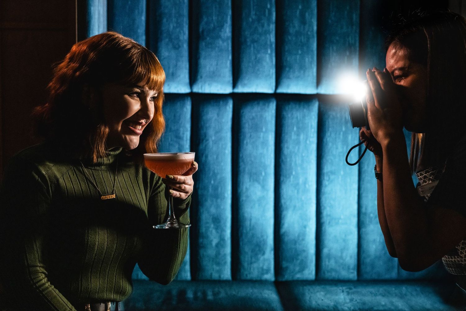 Two people enjoying cocktails in a dimly lit bar with blue curtains.