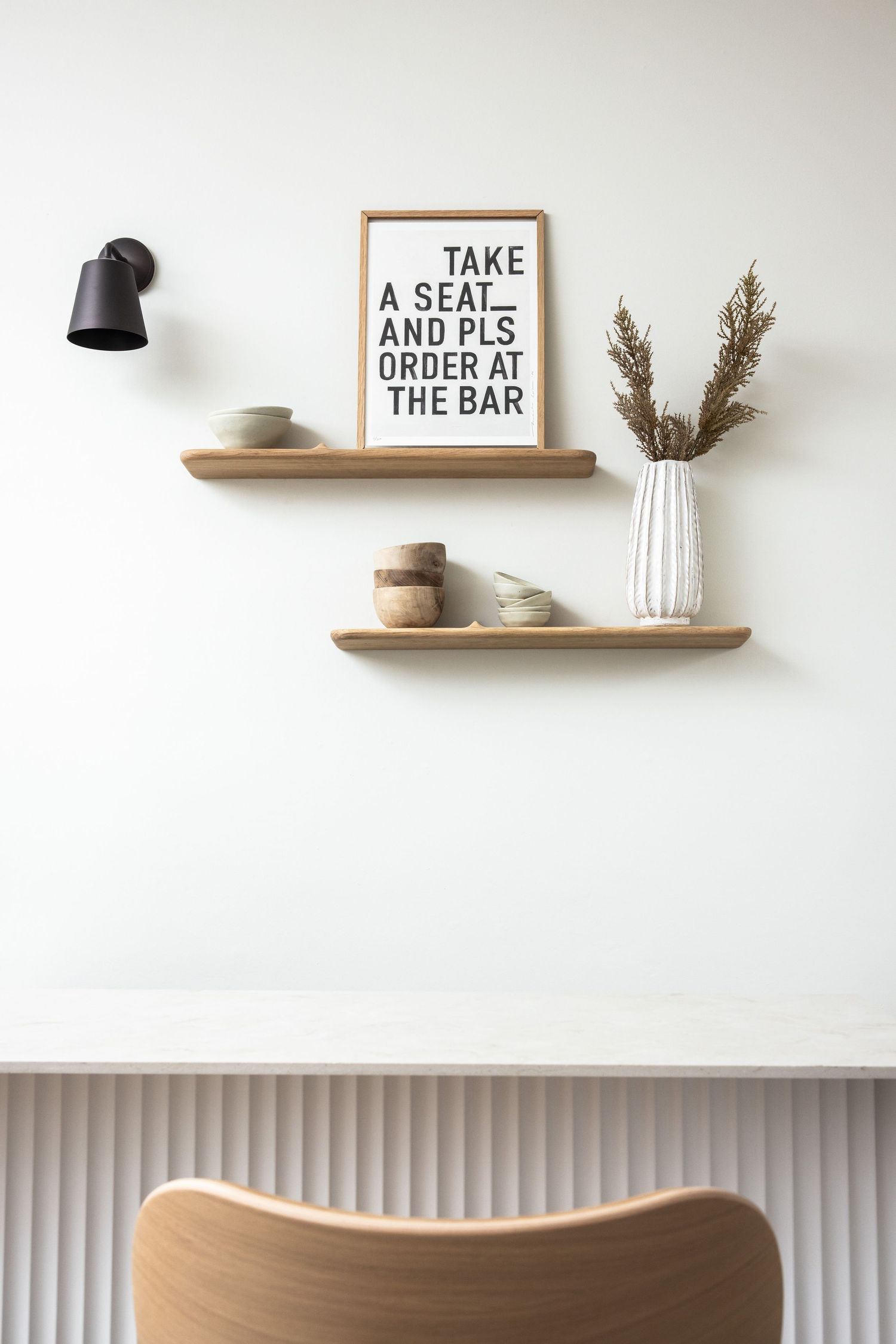 Minimalist wall shelves with decorative text signs and dried flowers against white wall.