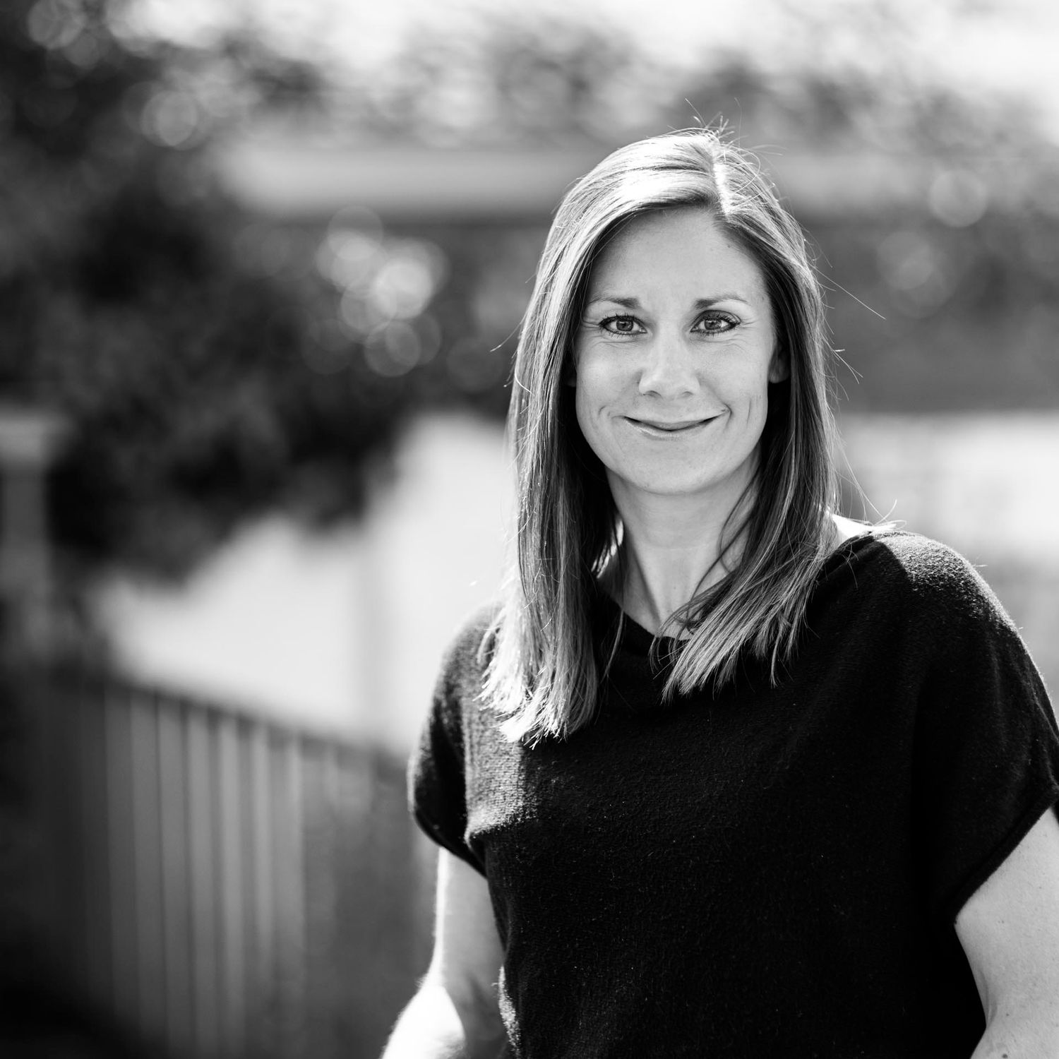 Black and white headshot of woman smiling outdoors with bokeh background.