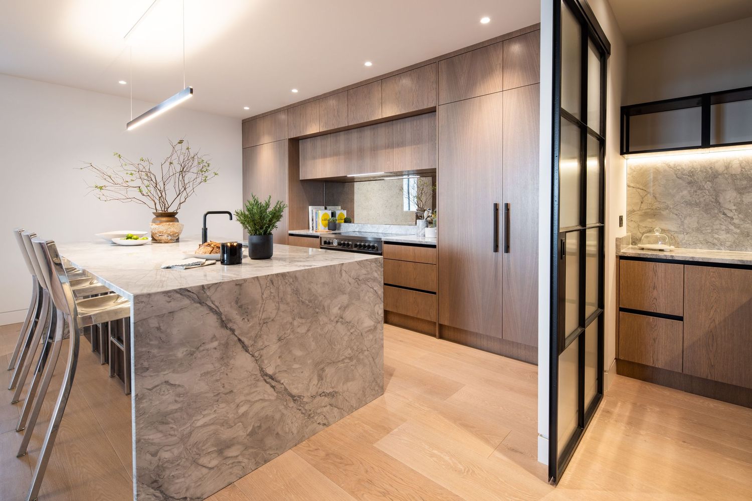 Modern kitchen featuring marble waterfall island, wood cabinetry, and minimalist design with natural light.