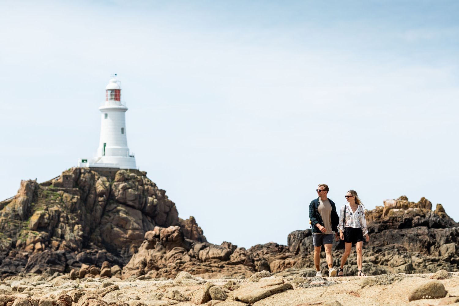 Hikers standing near white lighthouse on rocky coastal cliff.