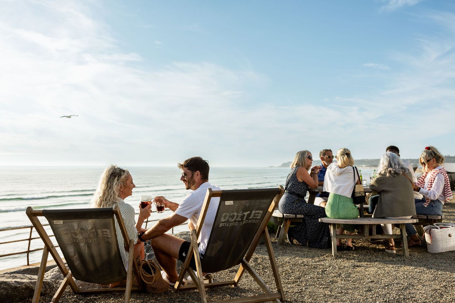 Beachside gathering with people relaxing in deck chairs at sunset.
