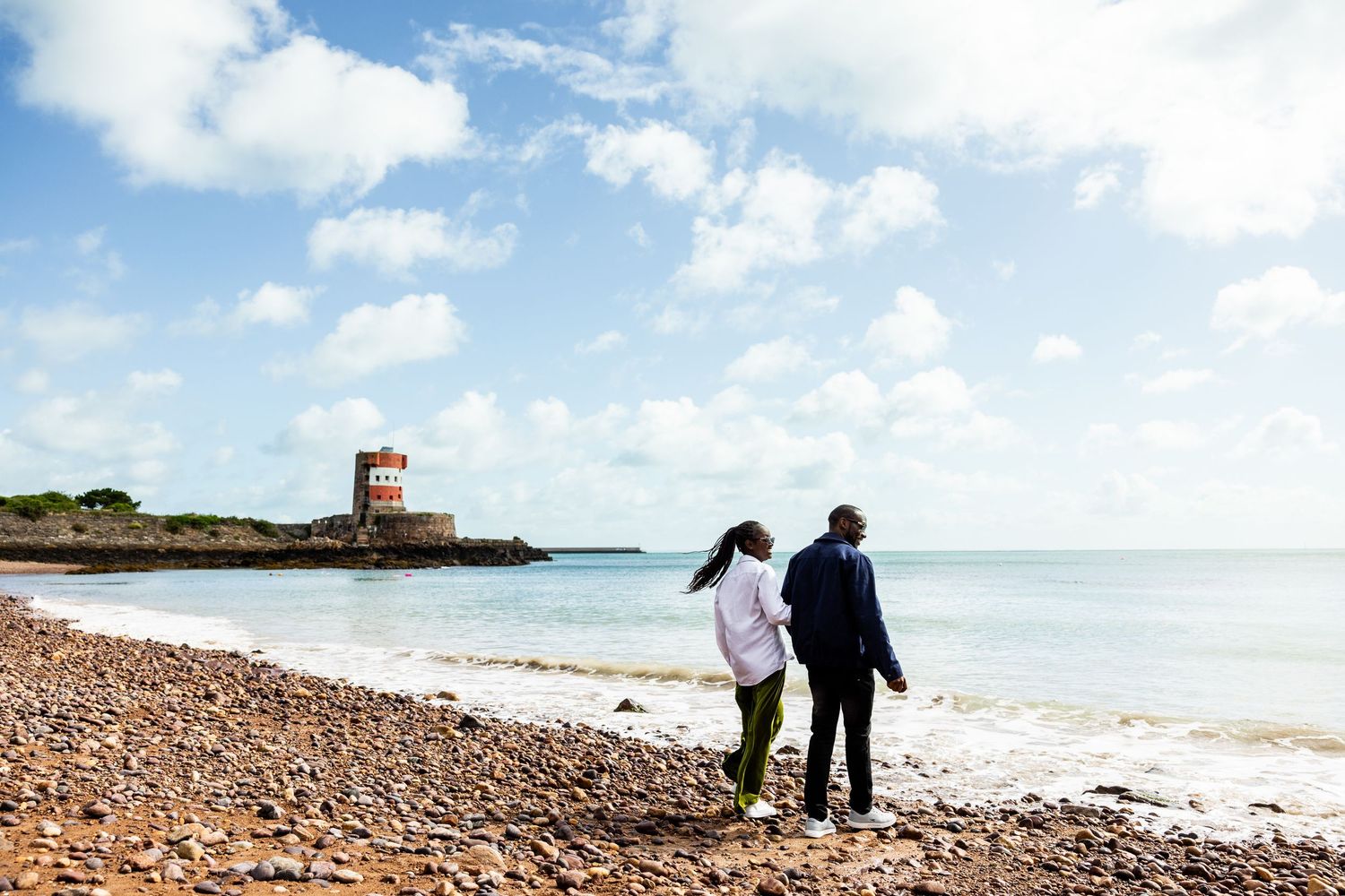 Peaceful coastal landscape with rocky beach and lighthouse in the distance.