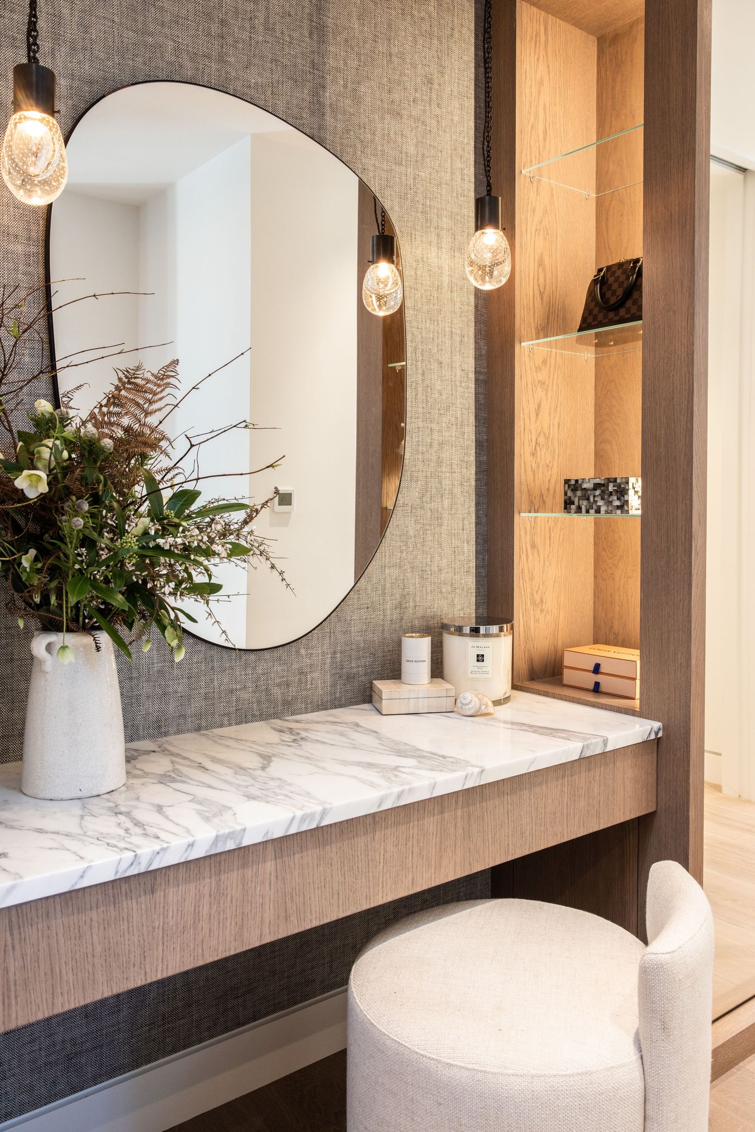 Elegant vanity area with round mirror, marble countertop, and floral arrangement in white vase.