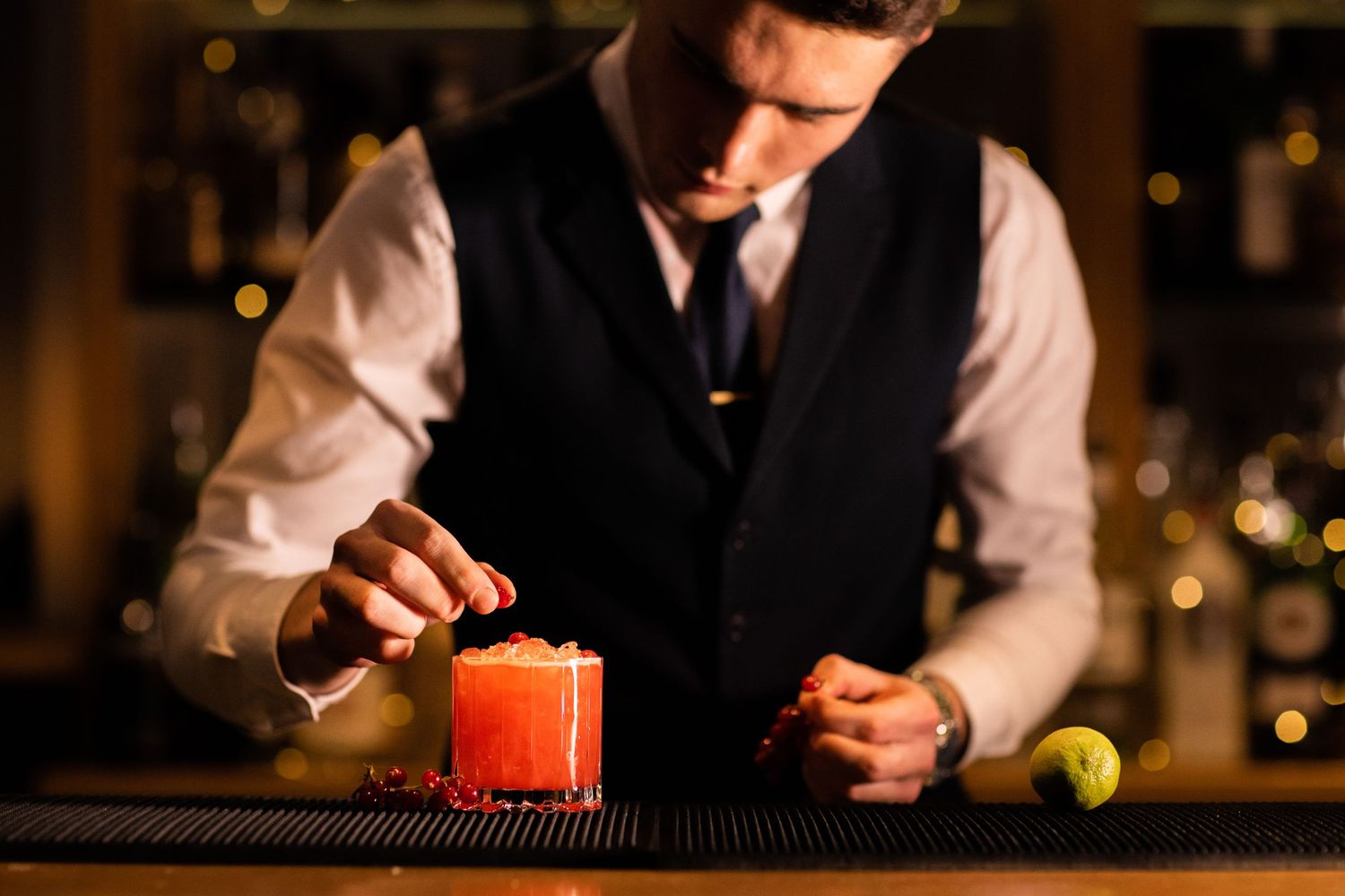 Bartender preparing craft cocktails at dimly lit bar counter.