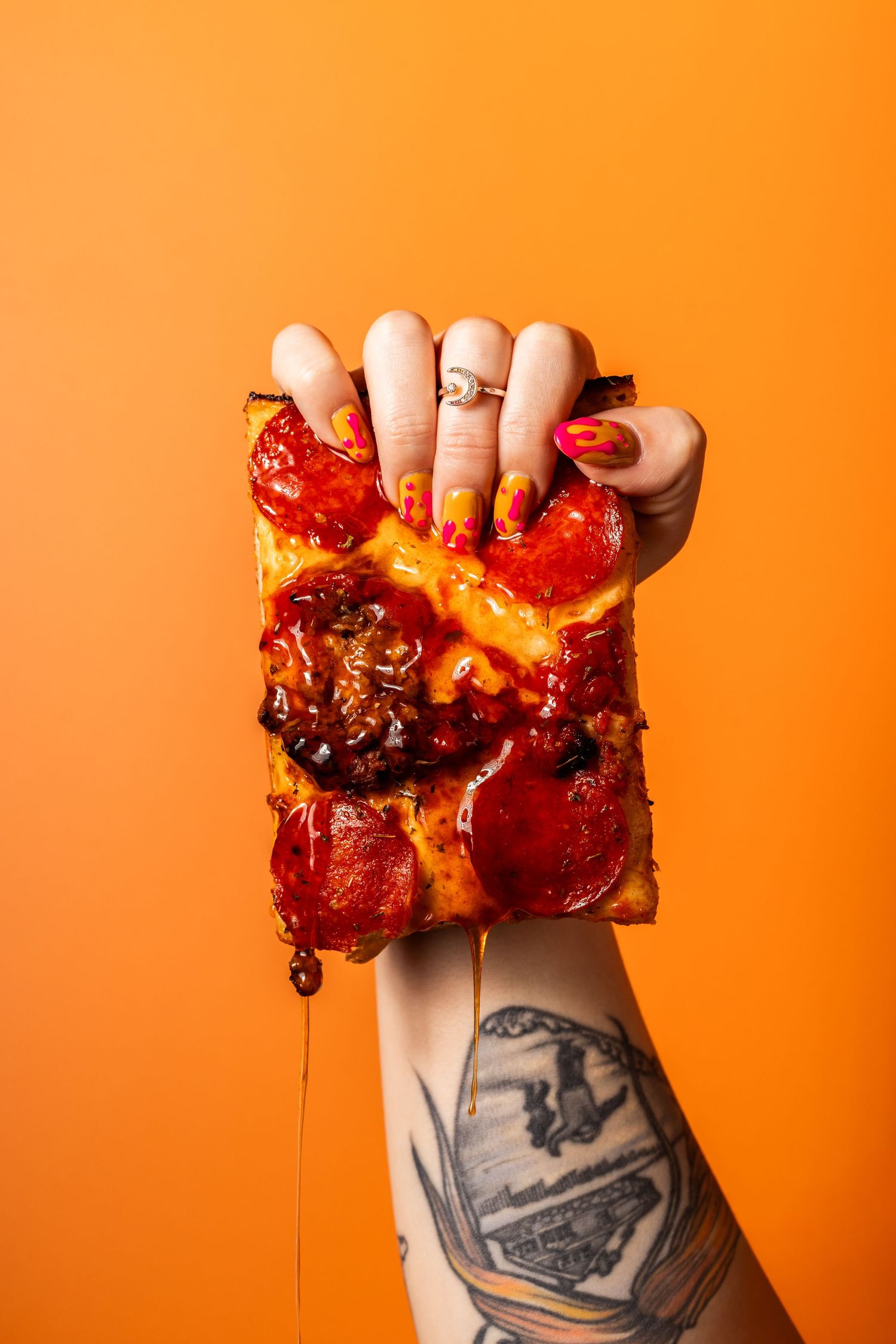 Messy pizza slice dripping with cheese and toppings against orange background.