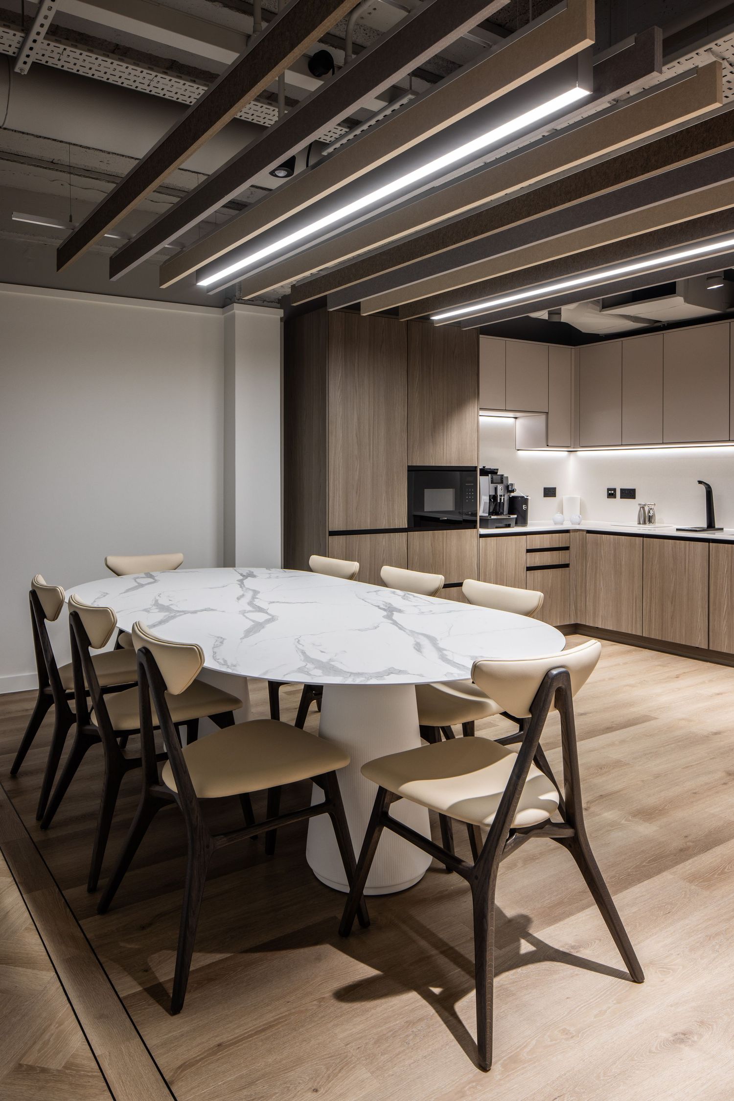 Modern conference room featuring a white marble table, black chairs, and wood-paneled walls.