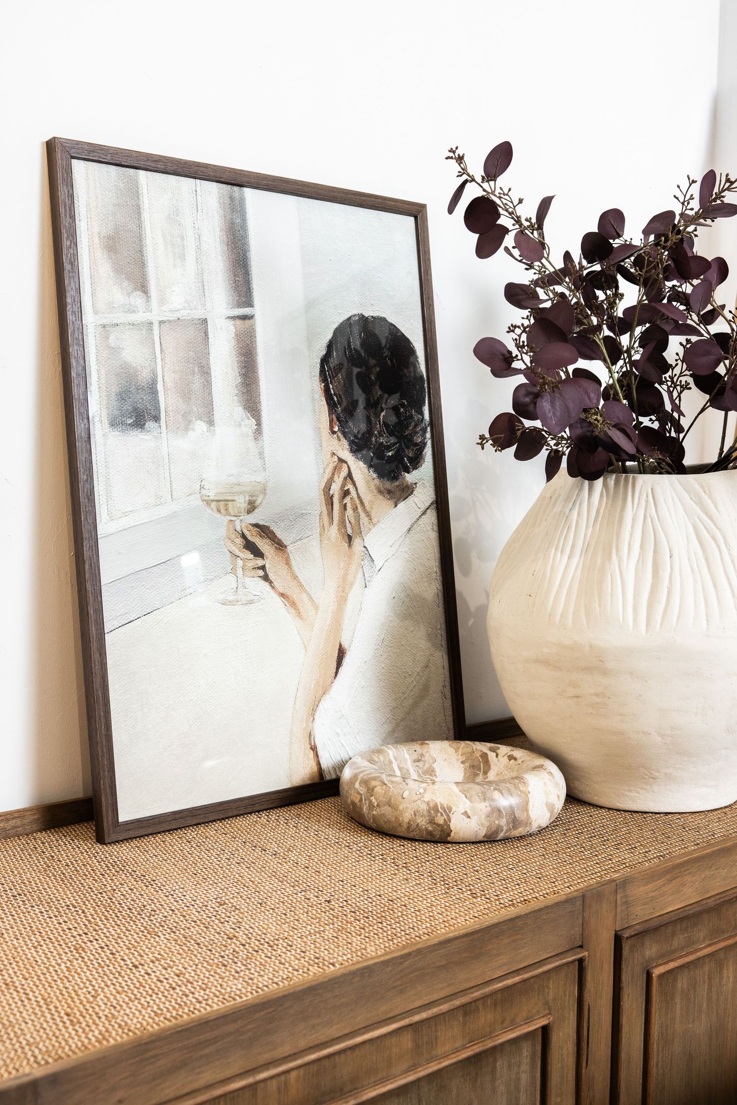 Artistic still life with framed photograph, cream vase with purple leaves on wooden console table.