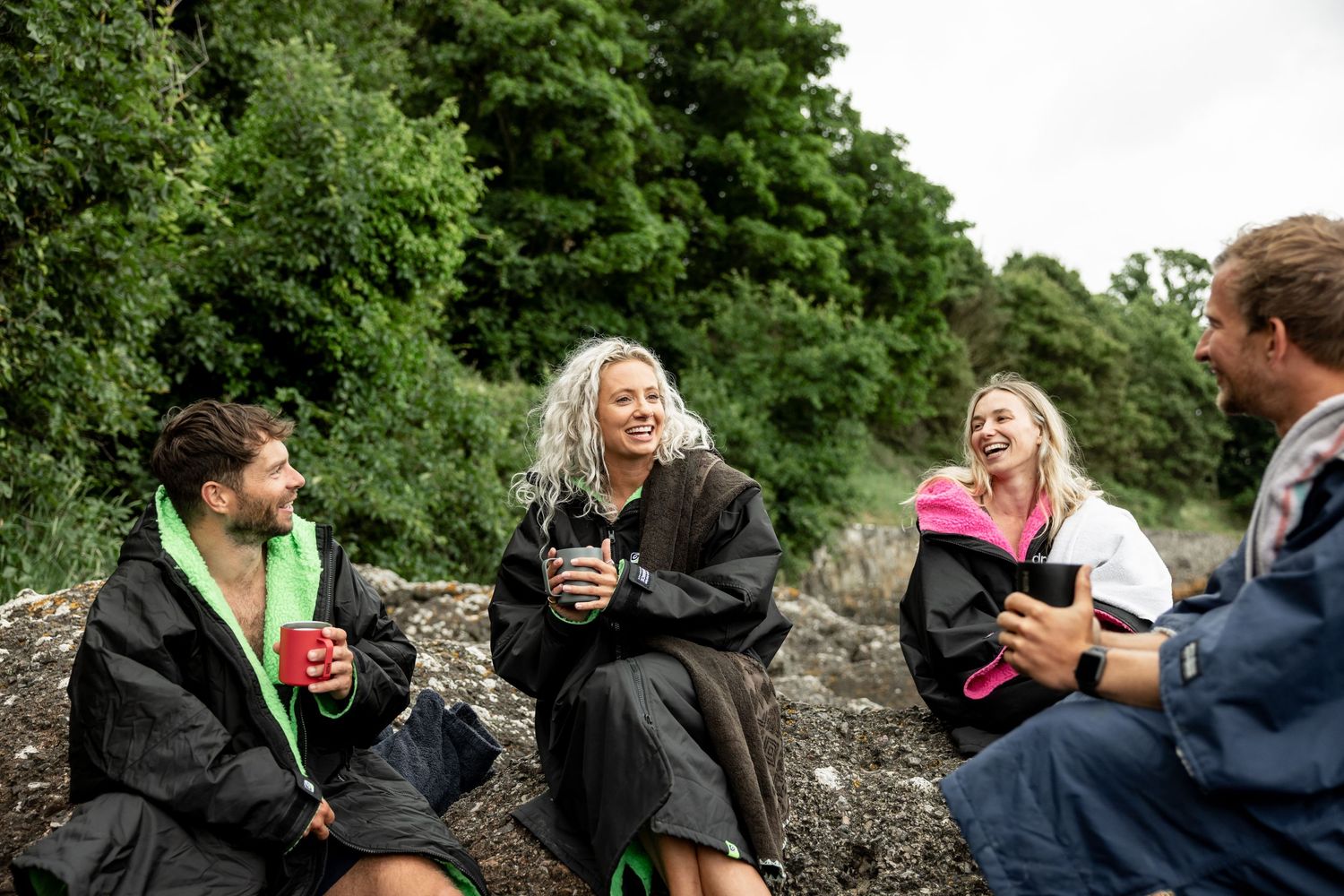 Friends enjoying drinks together while sitting on rocky coastal terrain.