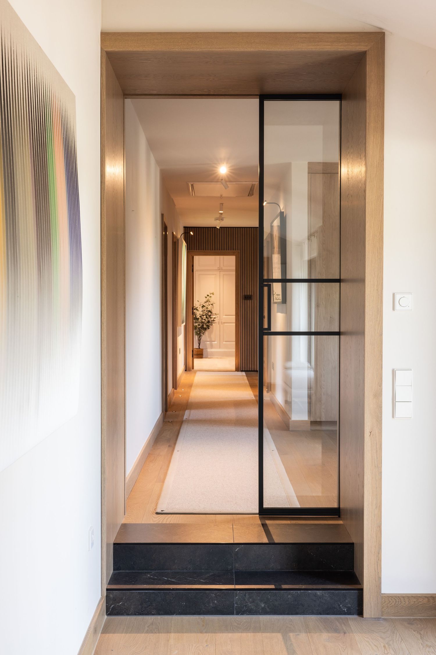 Contemporary hallway with glass partition door and black stone step detail.