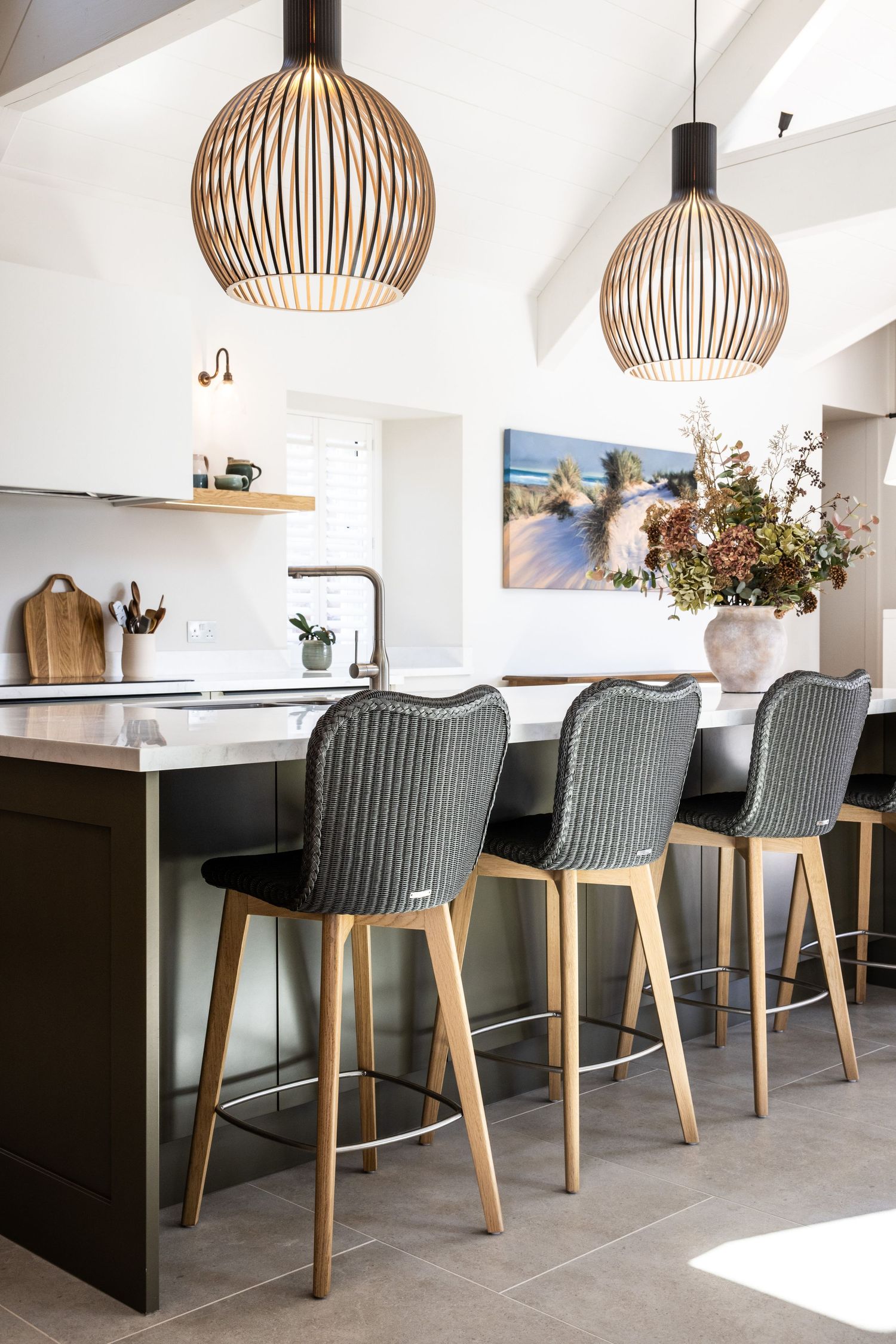 Sleek kitchen island with modern gray chairs and wooden pendant lights in an open concept space.
