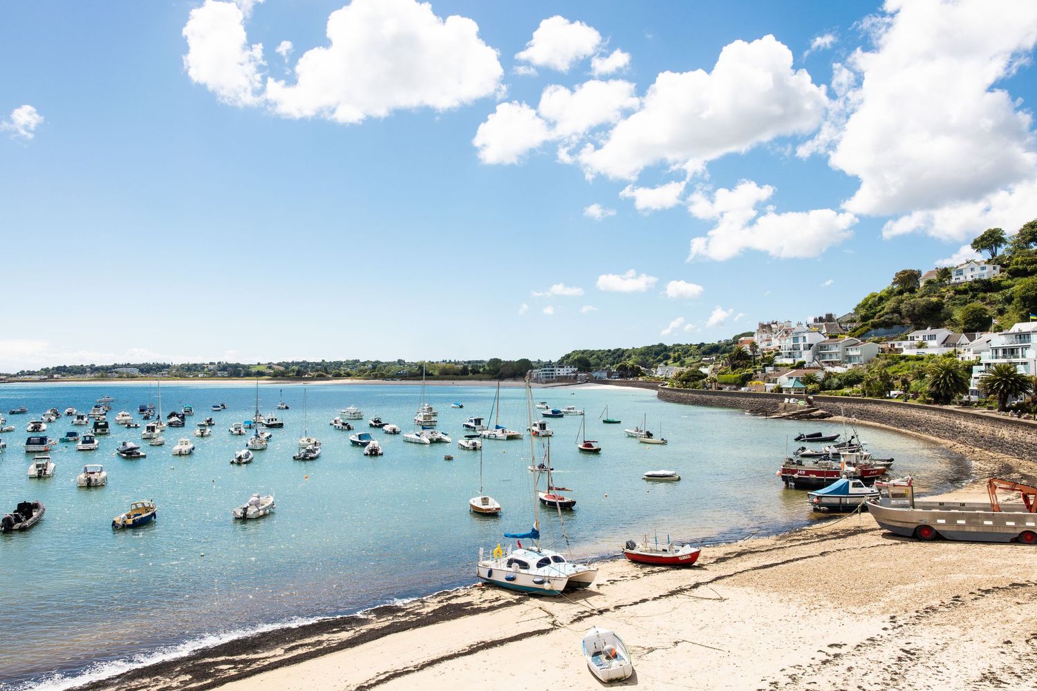 Panoramic view of boats anchored in a sunny harbor with blue sky and white clouds.