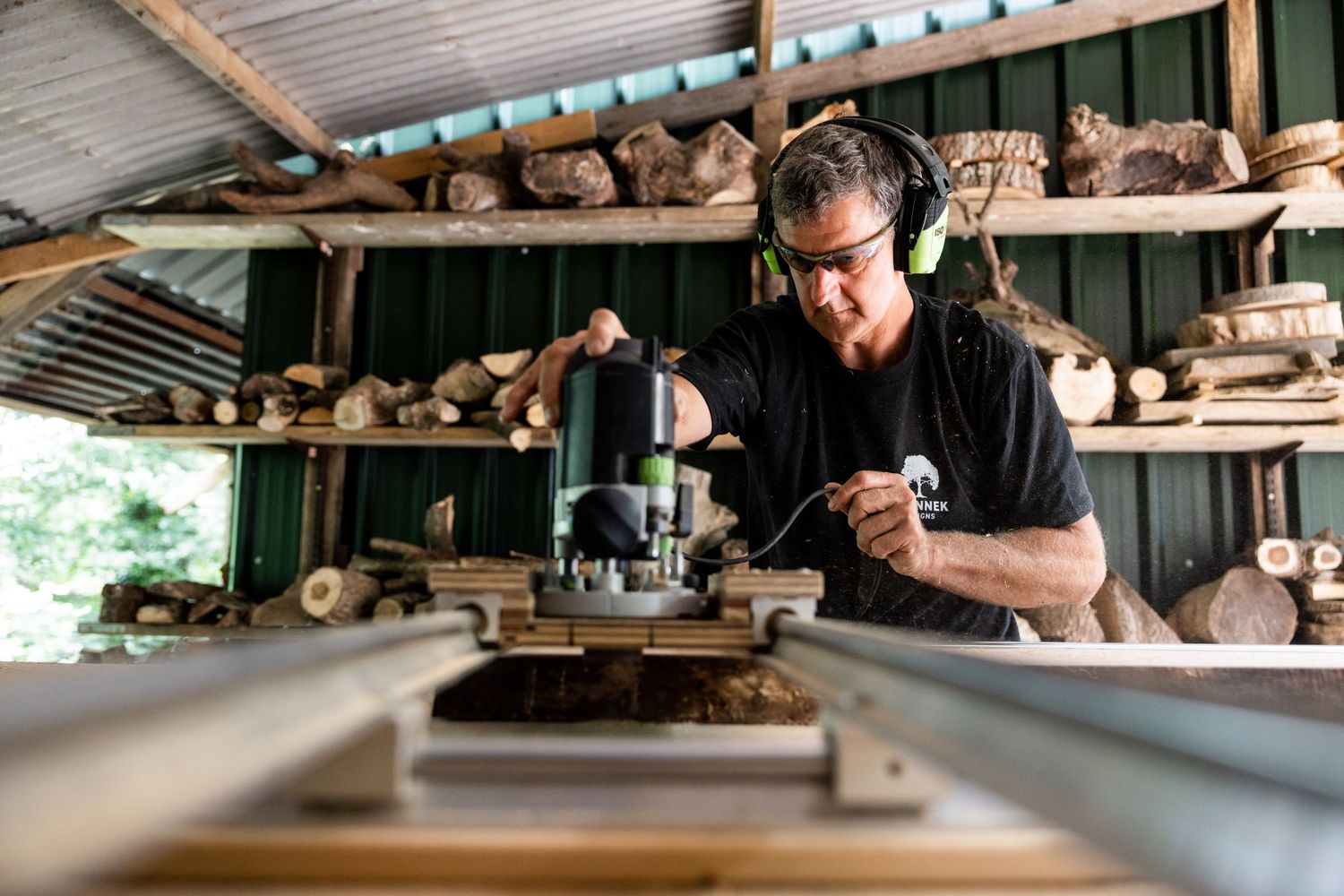 Person working in rustic woodshop with stacked lumber in background.