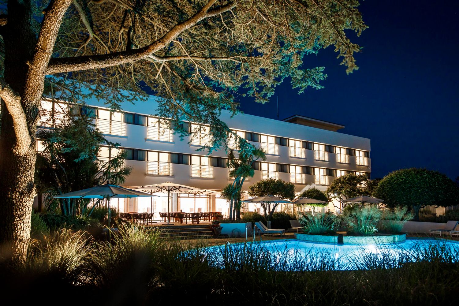 Luxury hotel exterior at night with illuminated pool and palm trees.