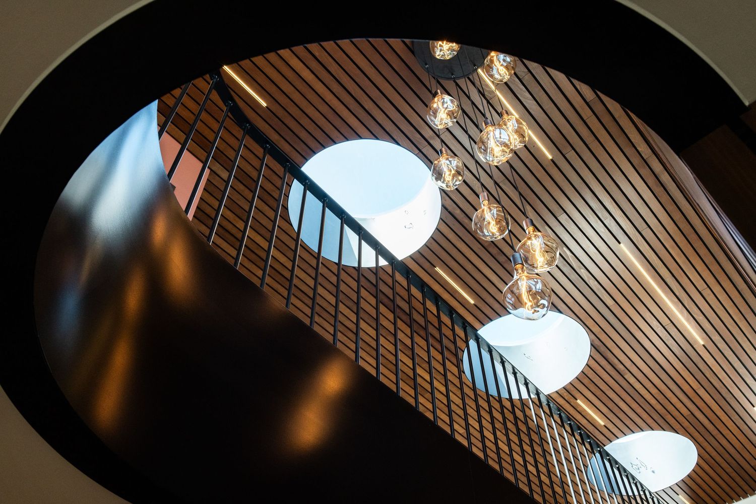 Wooden slat ceiling with circular skylights and modern lighting design.