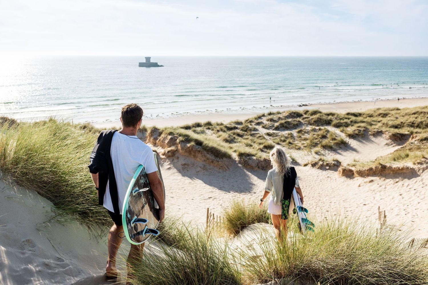 Scenic coastal view with sand dunes, beach grass, and ocean waves under blue skies.