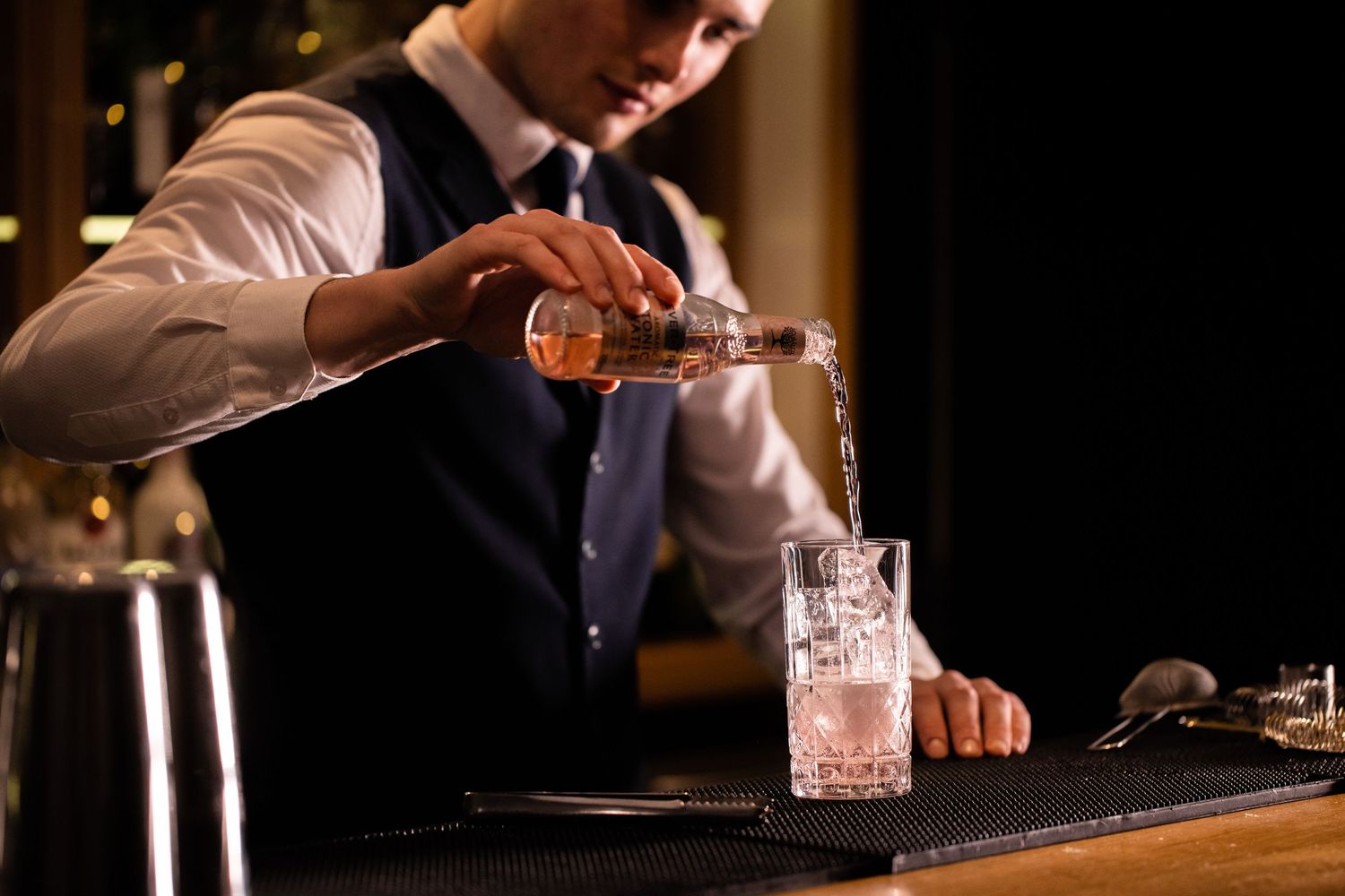 Bartender mixing drinks behind dark wooden bar counter.