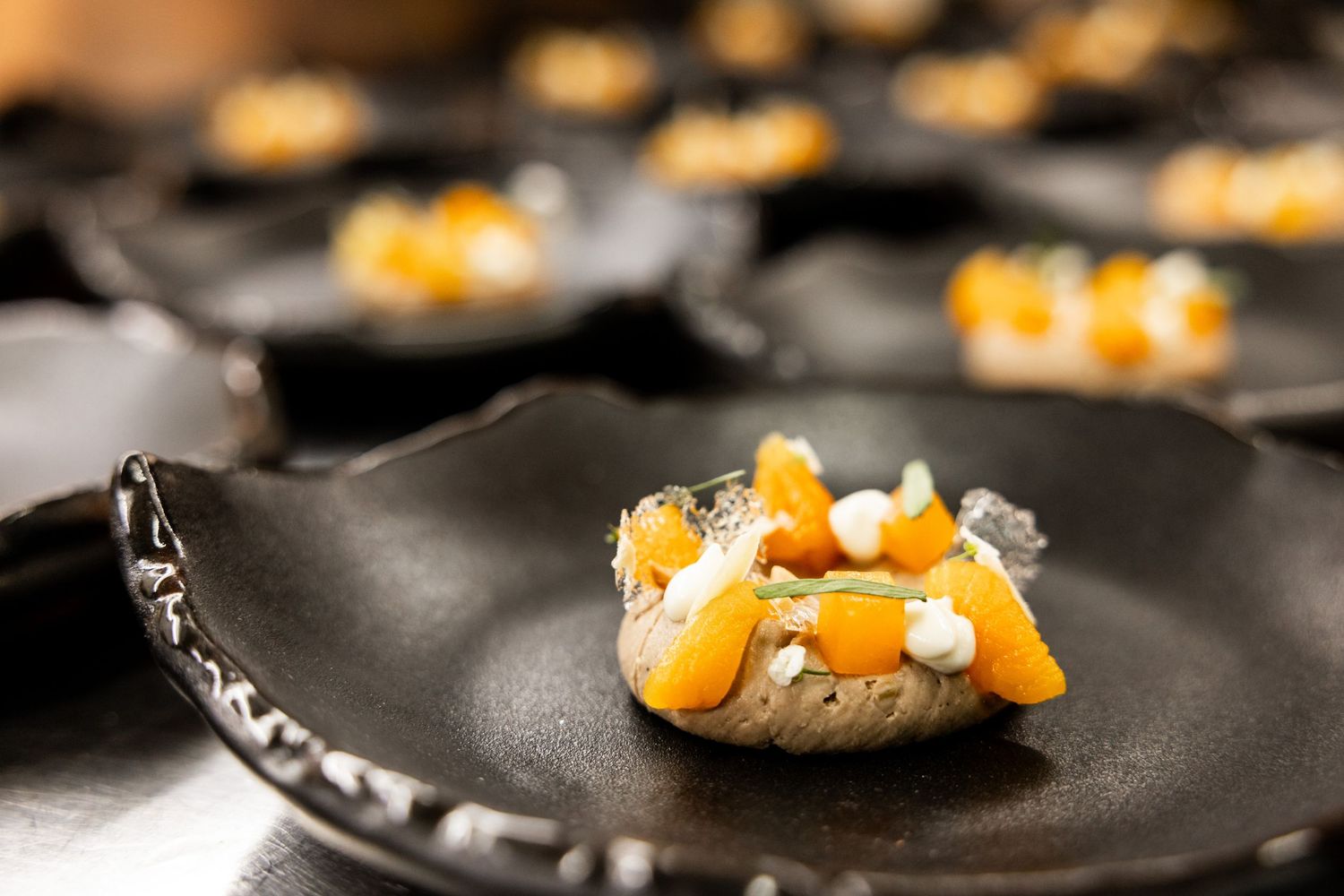 Delicate orange garnishes being carefully arranged on dark plates in a professional kitchen.