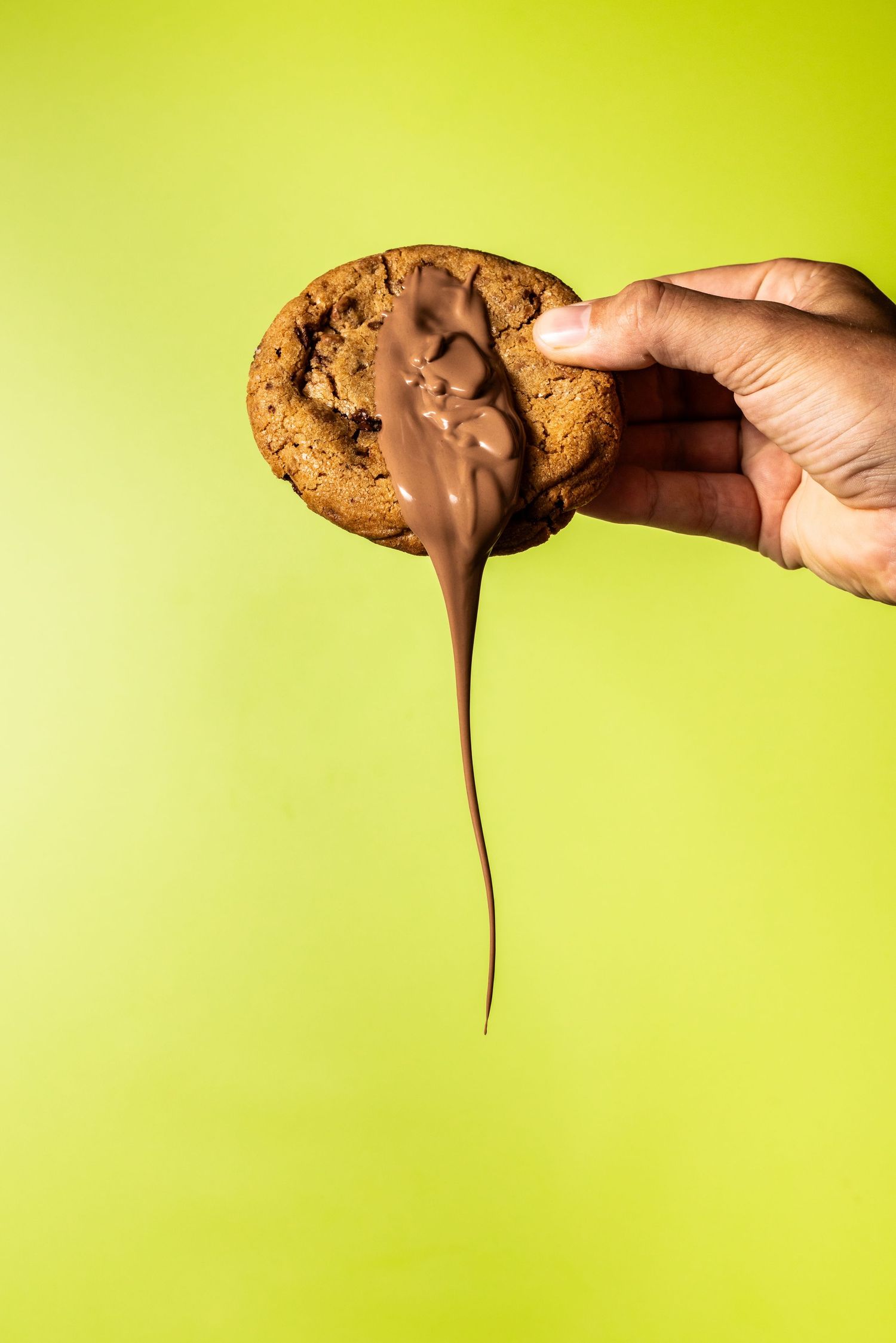 Chocolate sauce dripping dramatically from a cookie against lime green background.