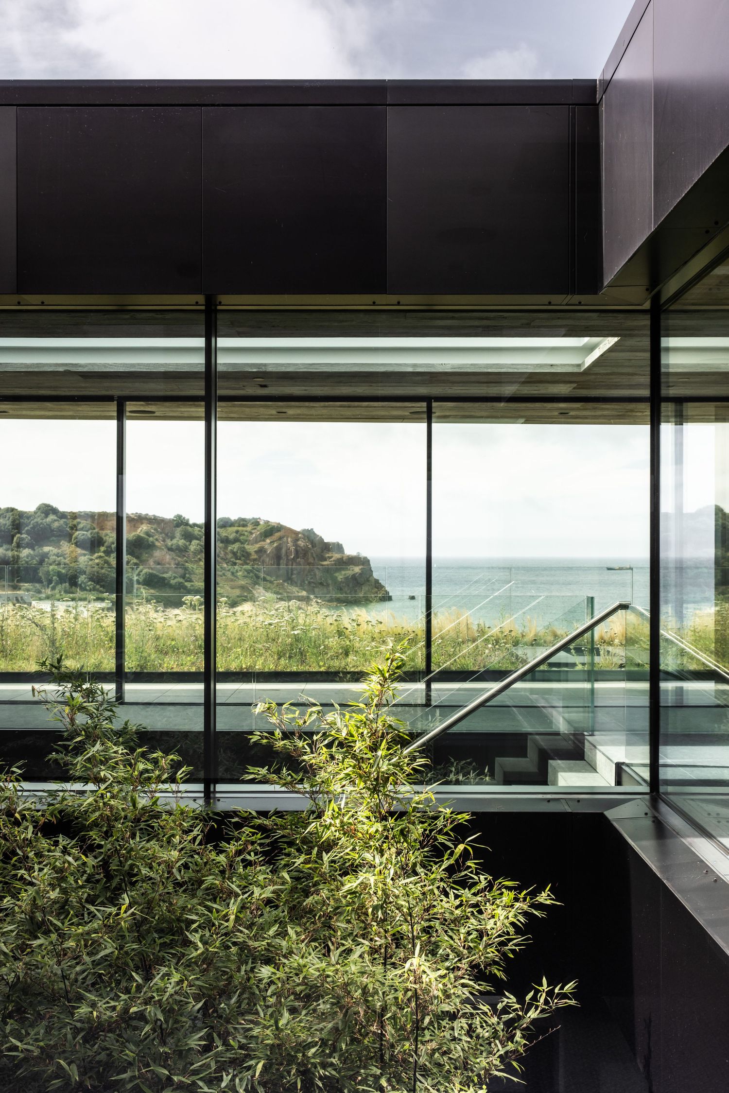 Floor-to-ceiling windows offering panoramic coastal views with lush greenery in the foreground.