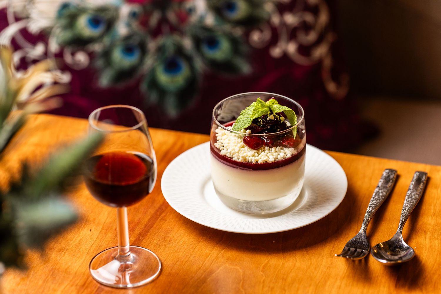Artfully presented desserts and wine glasses on a wooden table with decorative peacock feathers.