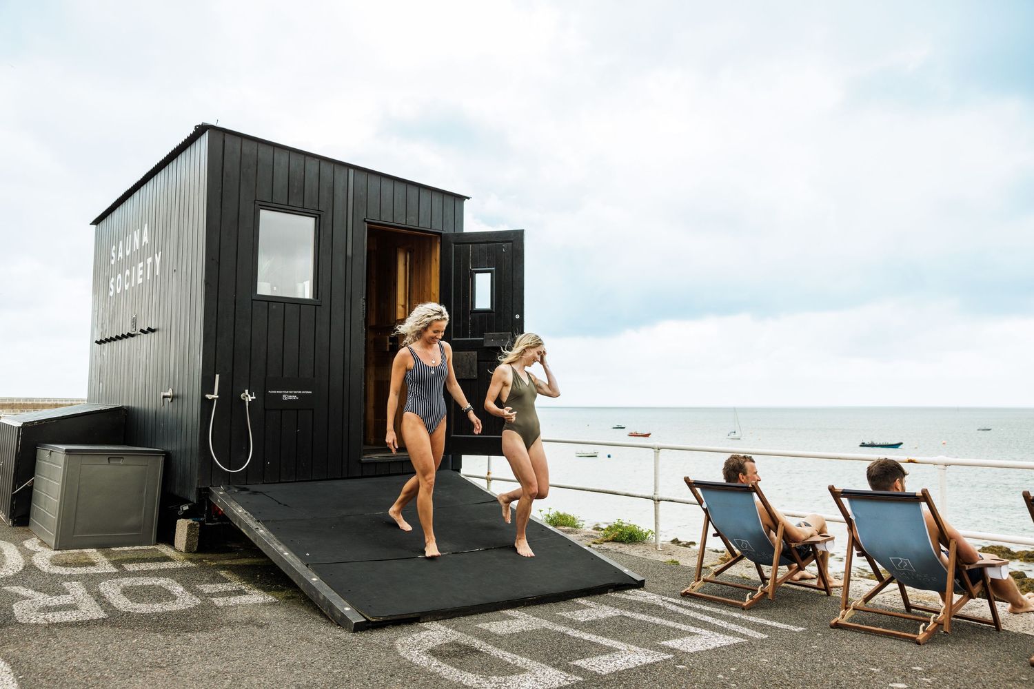 Modern black beach cabin with outdoor shower and lounge chairs.