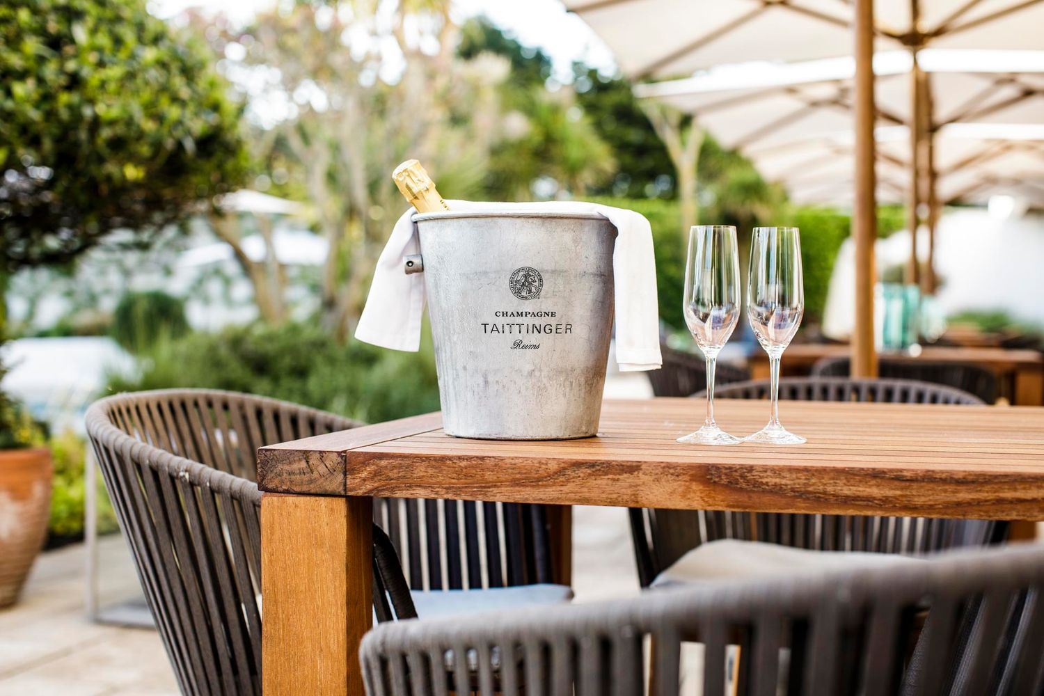Champagne bucket and glasses on wooden table at outdoor restaurant.