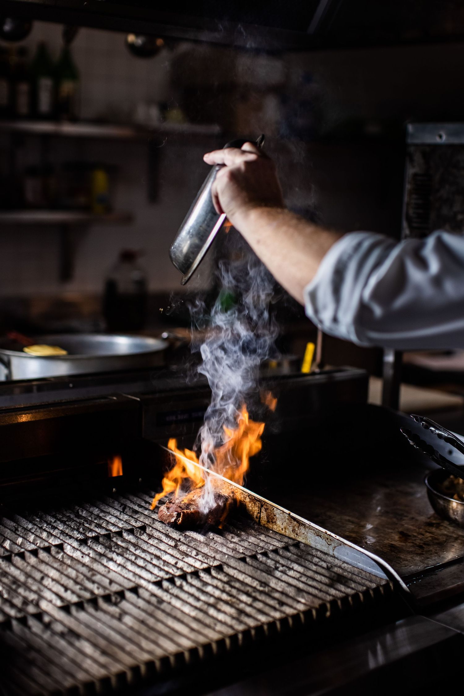 Flames and smoke rising from a professional grill during cooking service.