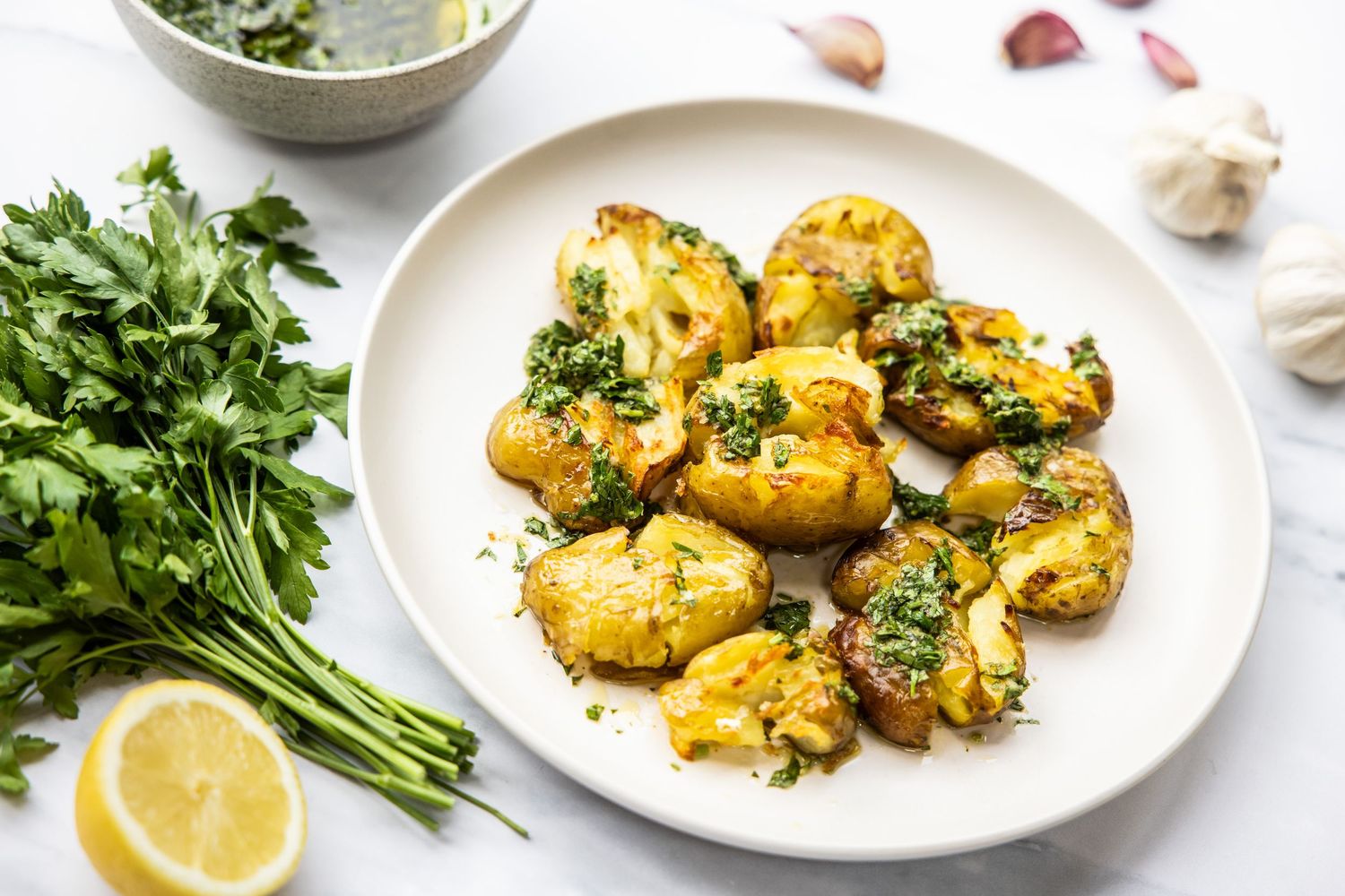 Golden roasted potatoes garnished with fresh parsley and lemon on white plates.