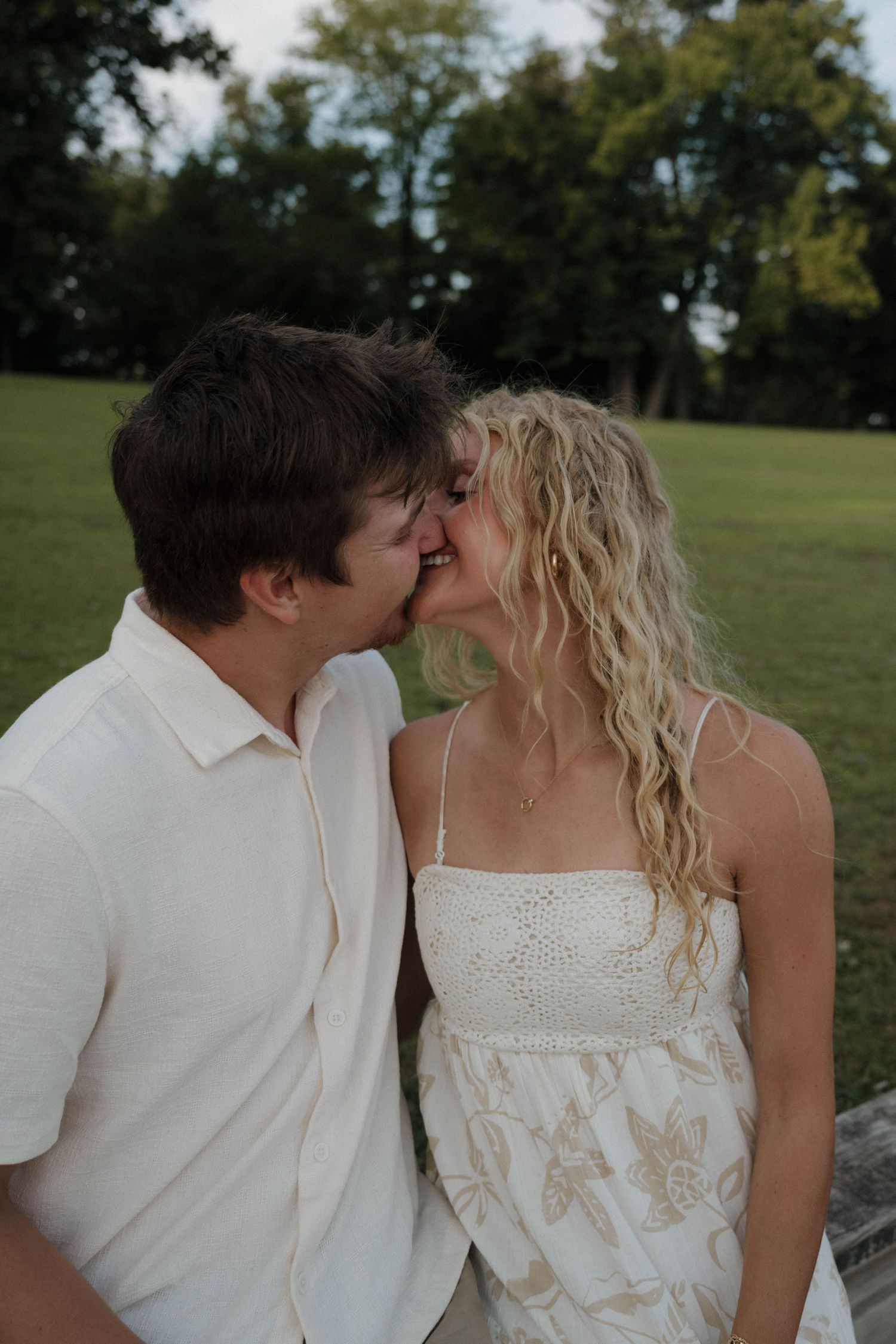 Young couple about to kiss outdoors, woman in floral sundress and man in white shirt in park.