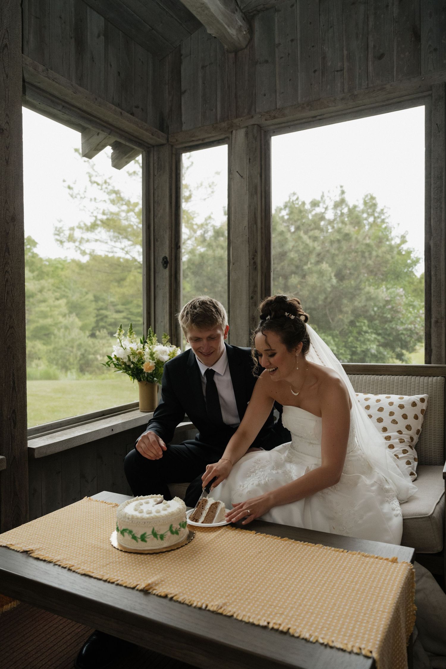 Bride and groom cut wedding cake inside rustic wooden cabin venue.