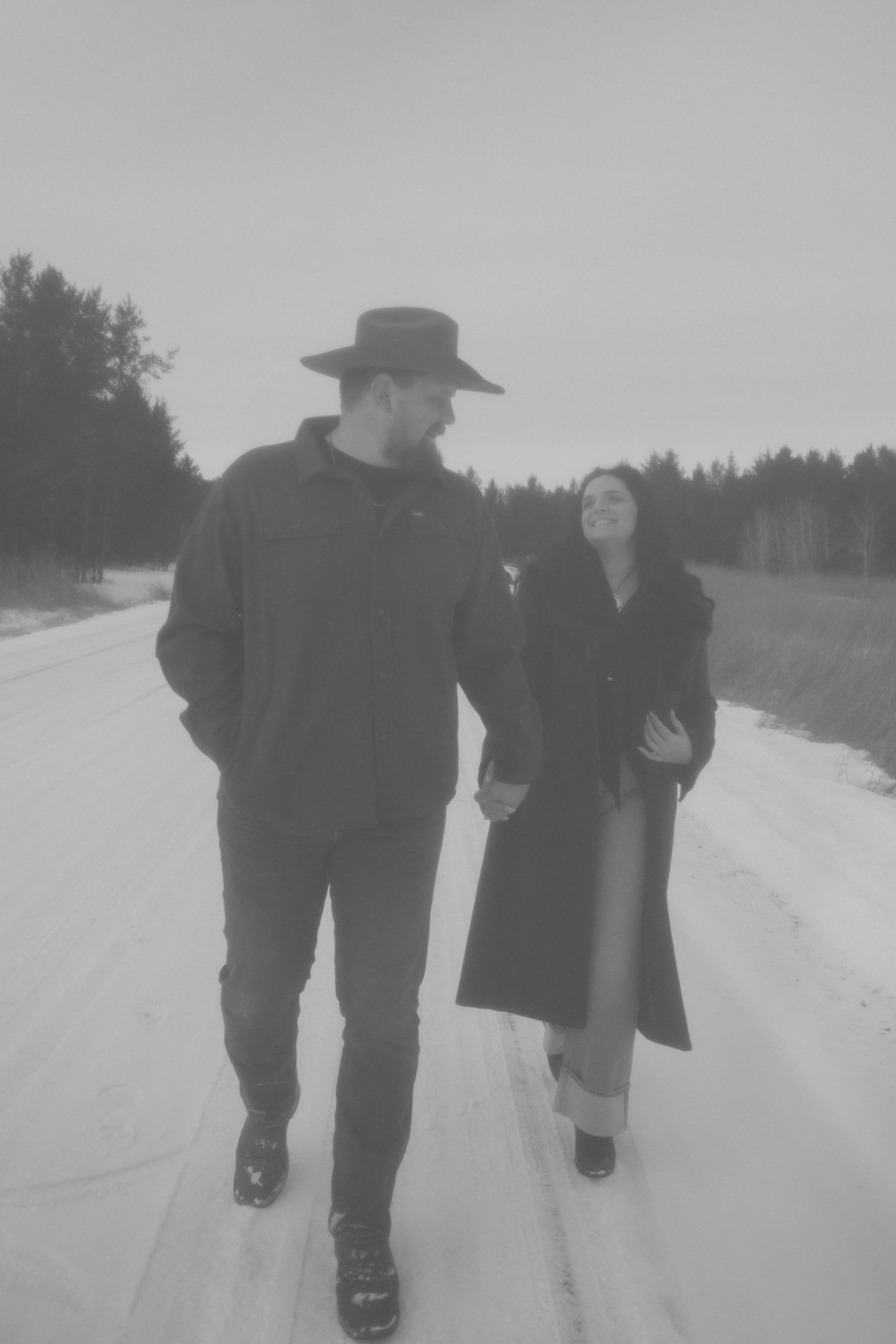 Black and white photo of couple walking hand in hand on a snowy road.