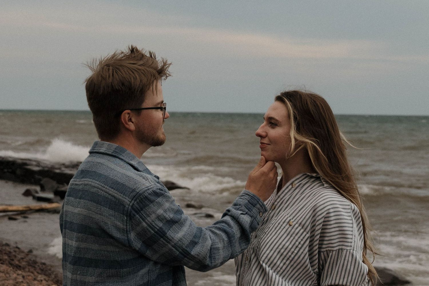 A man gently touches a womans face as they share an intimate moment on a rocky shoreline.