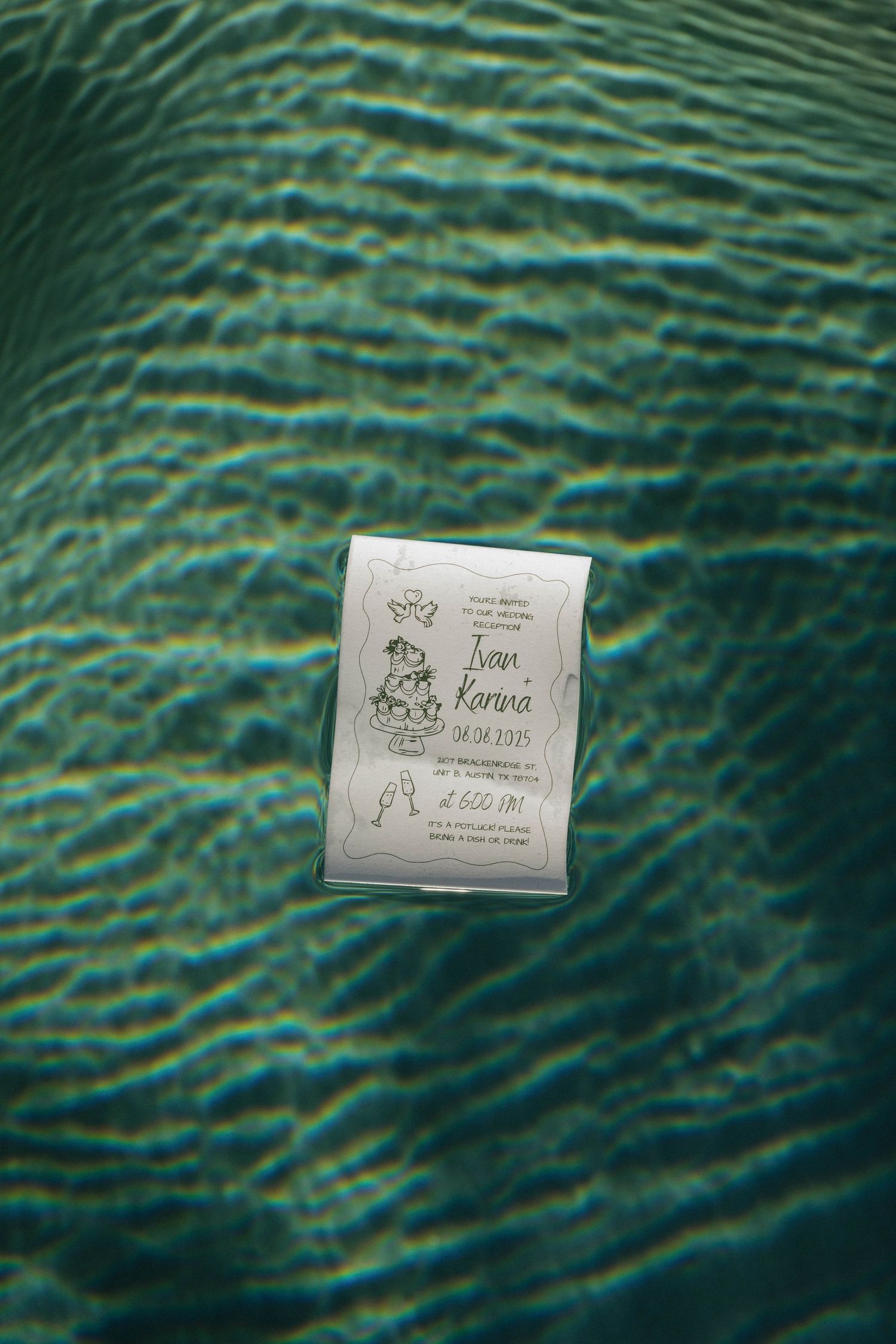 A wedding invitation for Ivan and Kenna floats in shimmering turquoise water.