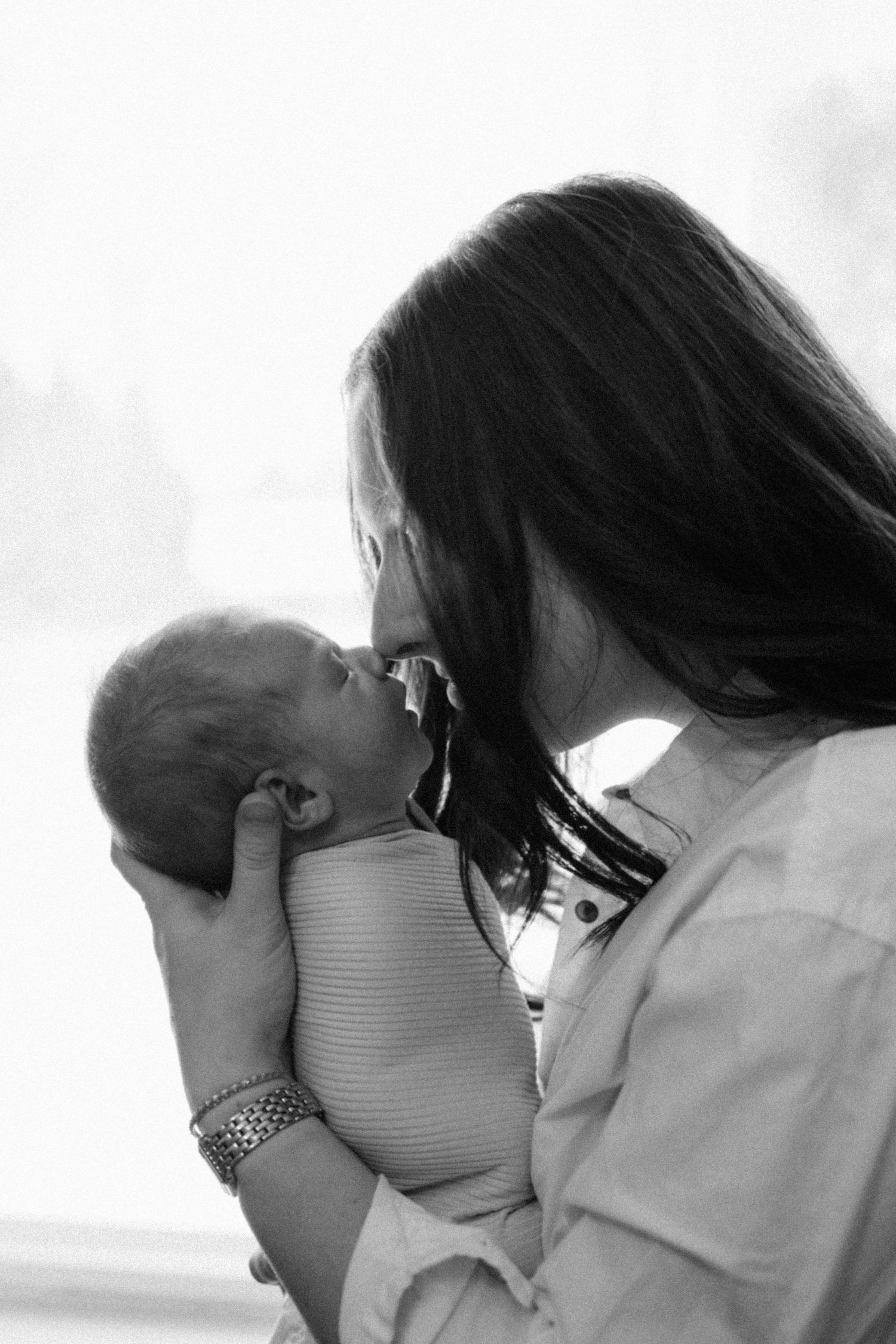 Black and white photo of mother tenderly kissing her newborn baby.