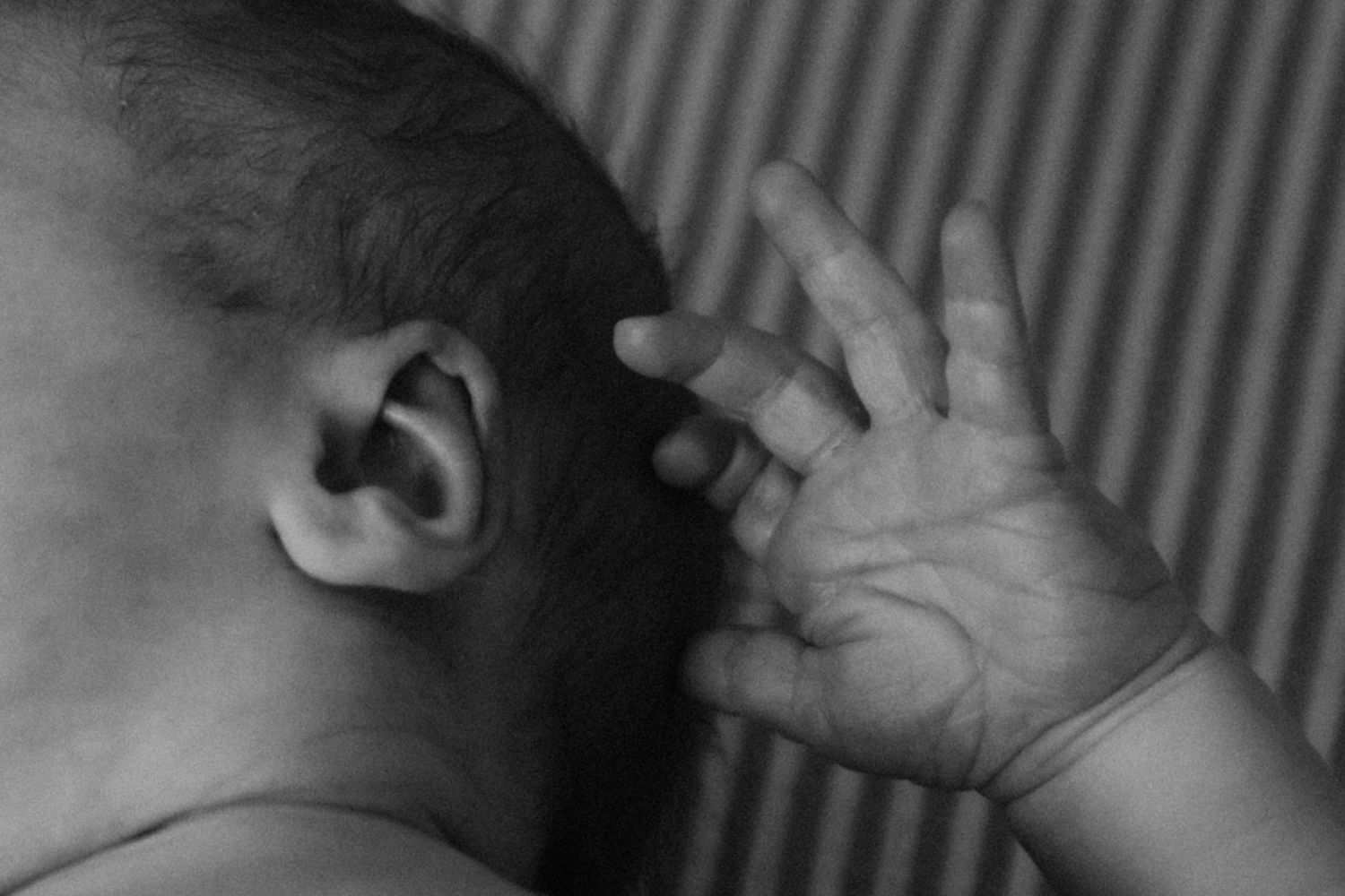 Close-up black and white photo of a newborn baby's ear and tiny hand.