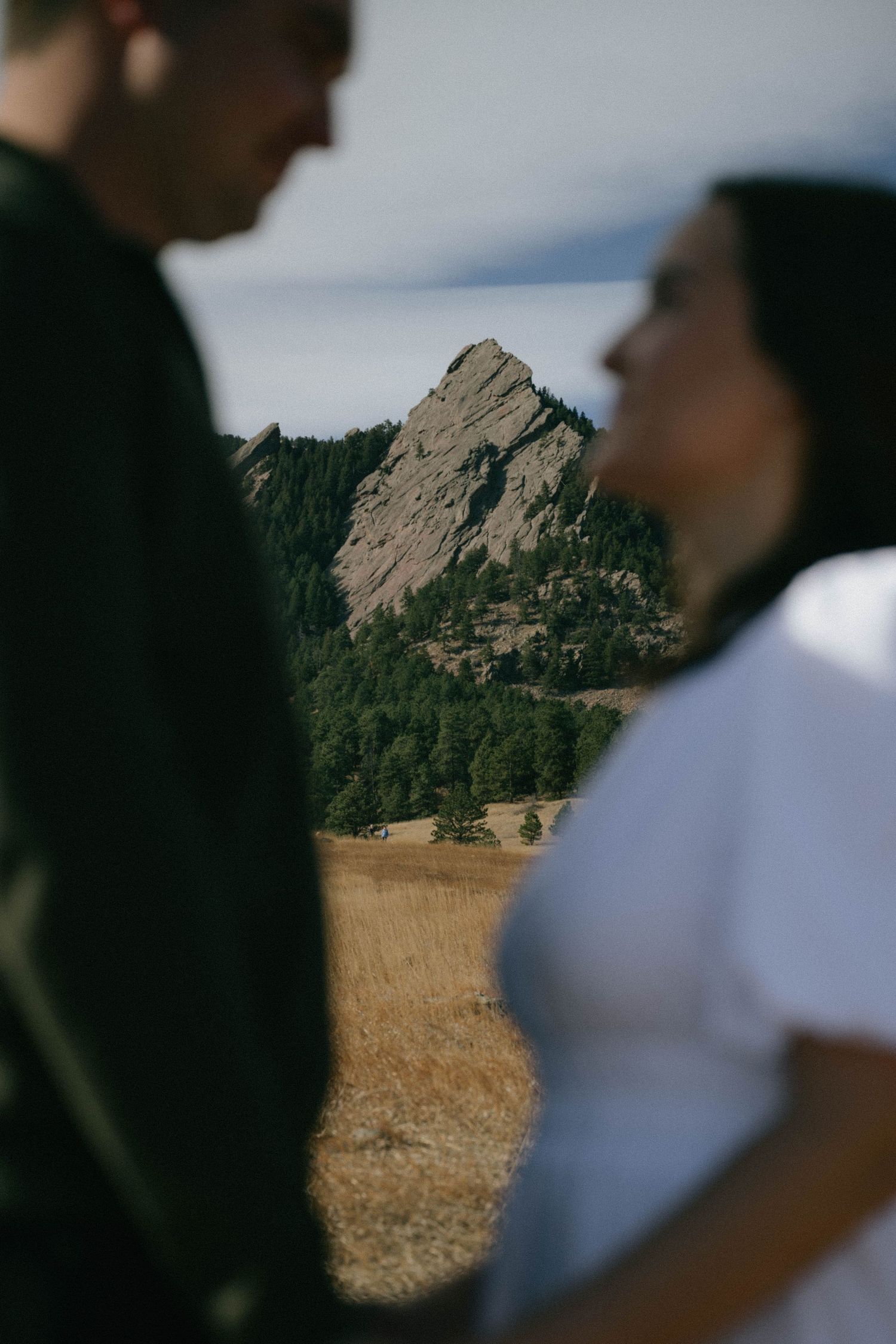 Couple faces each other with iconic Flatiron rock formation visible between them in soft focus.