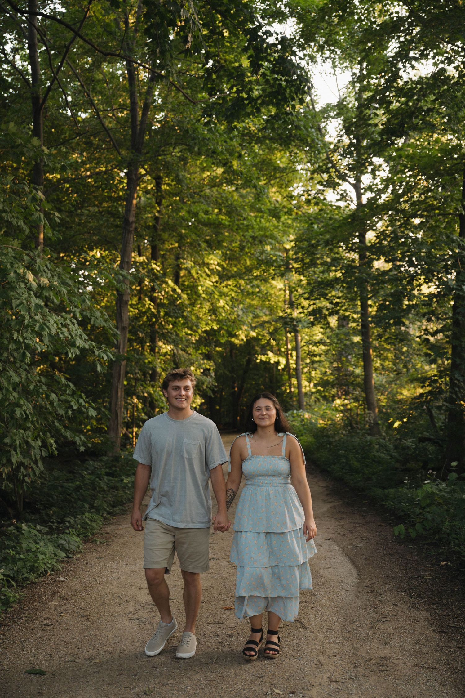 Young couple walking hand in hand down a tree-lined path in golden summer light.