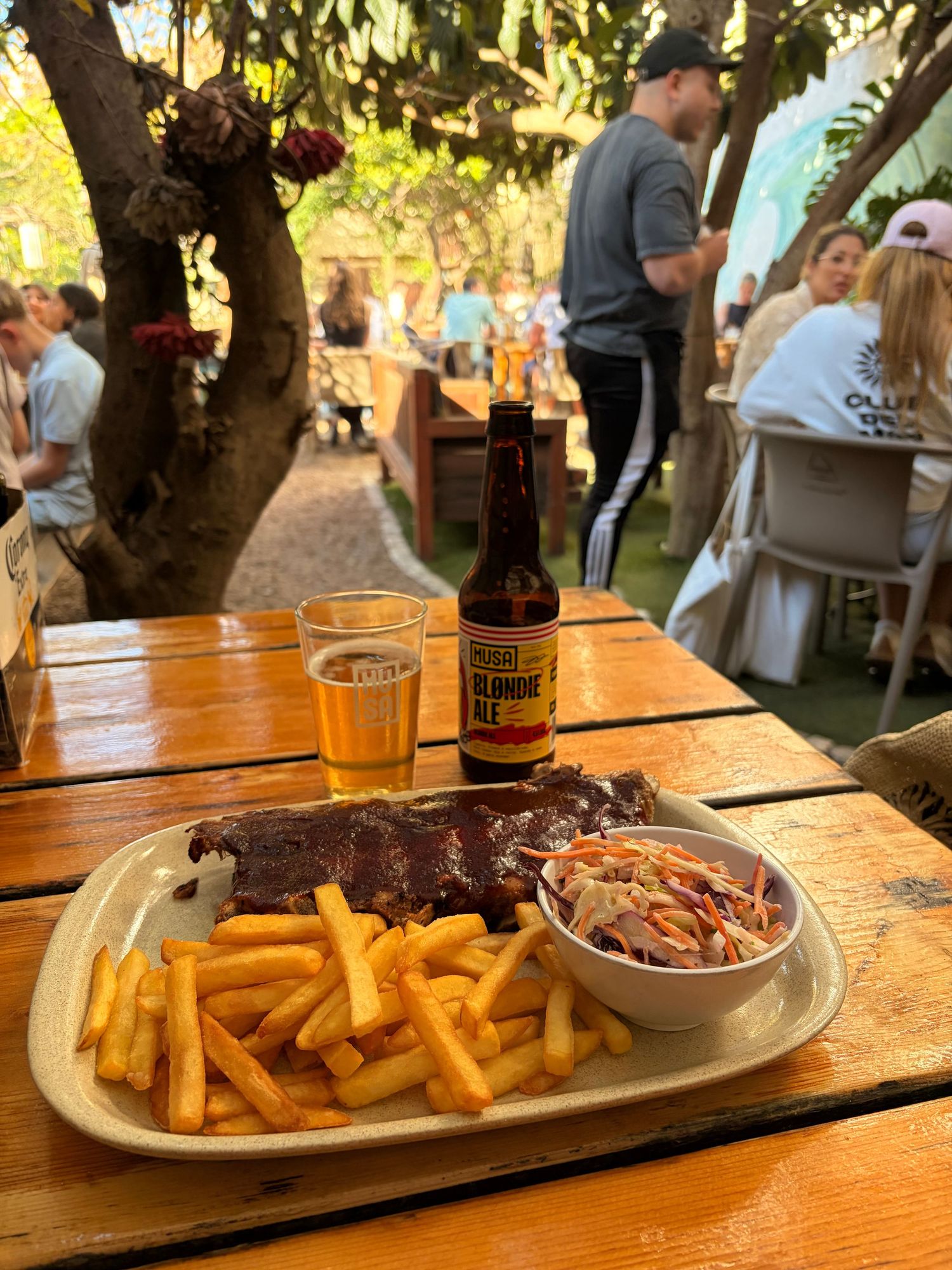 Plate of BBQ ribs with fries and coleslaw served with craft beer at outdoor garden restaurant.