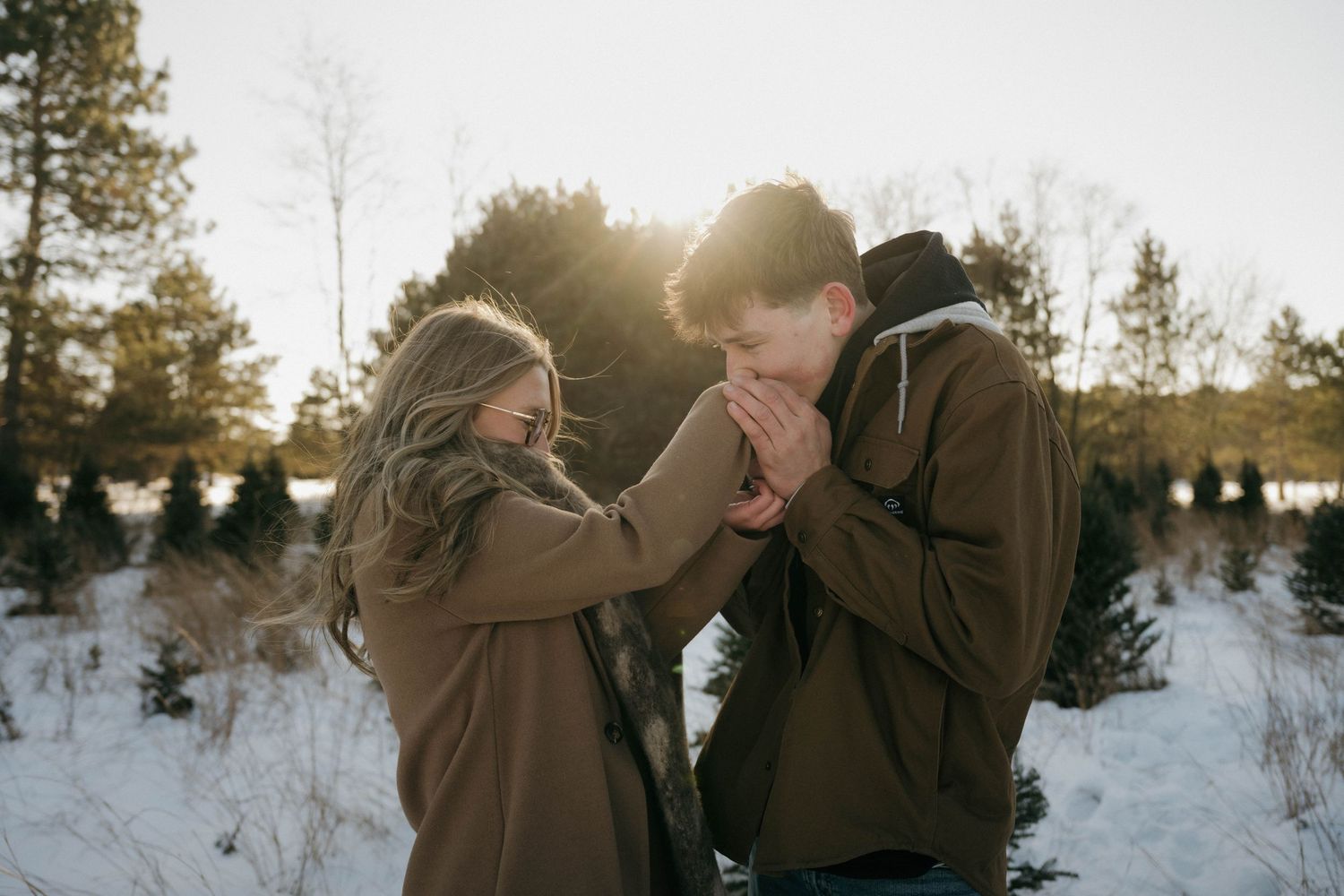 Couple holding hands warmly together in a snowy winter forest at sunset.