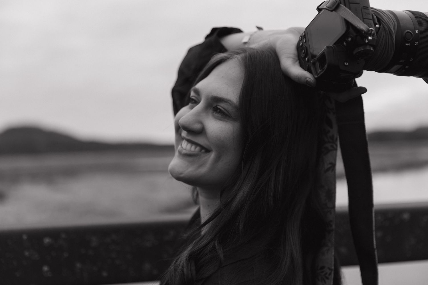Black and white portrait of smiling woman photographer with camera strap outdoors.