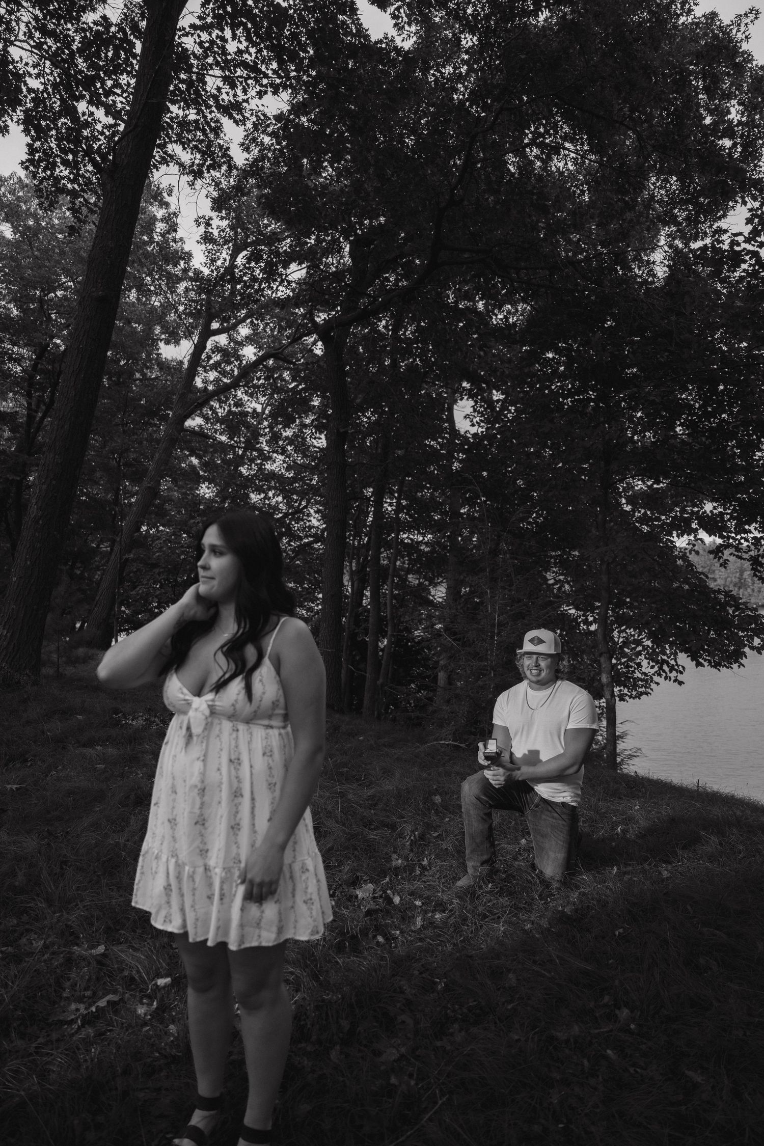 Black and white photo of man kneeling proposing to woman in forest.