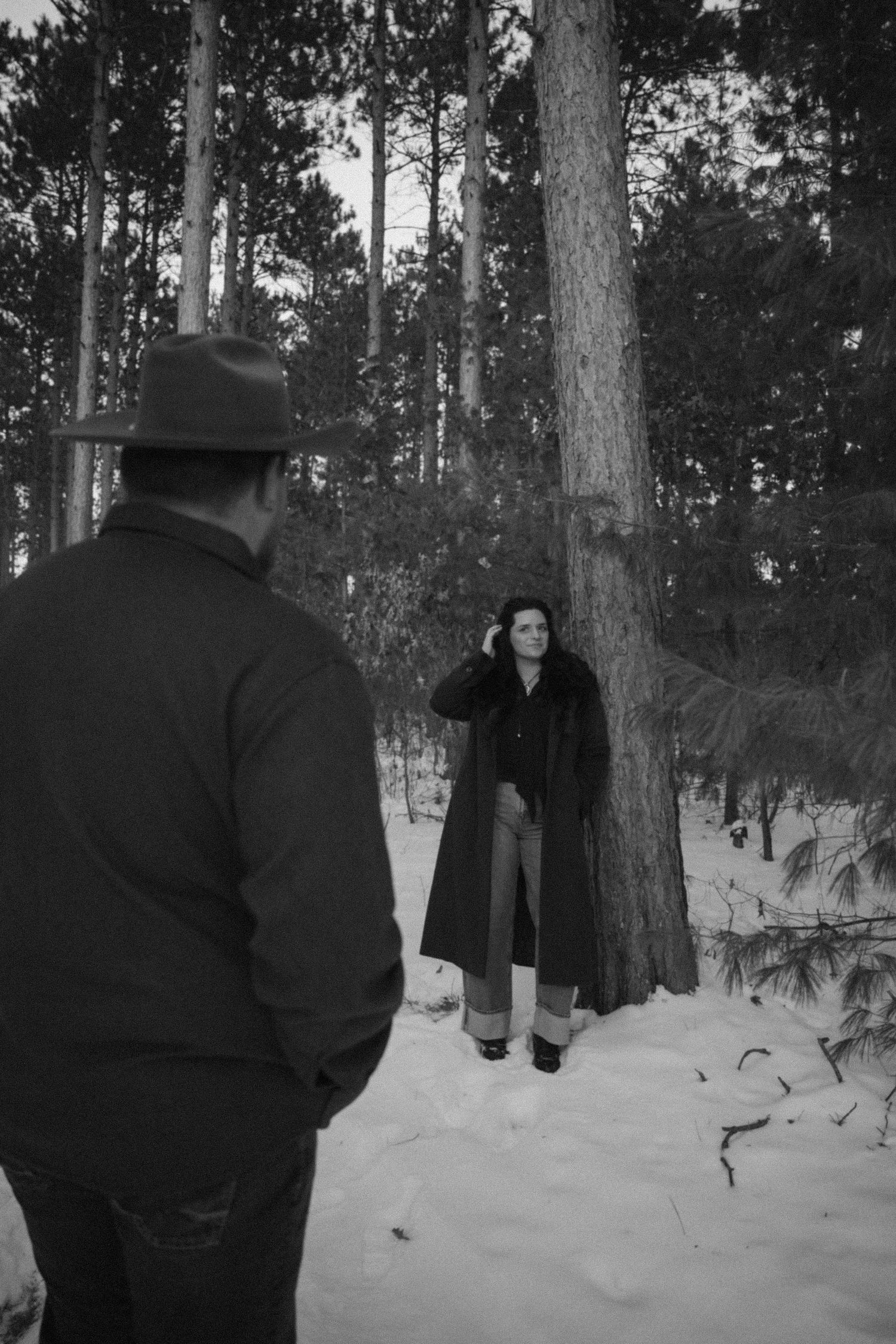 Black and white photo of couple in a snowy pine forest during winter.