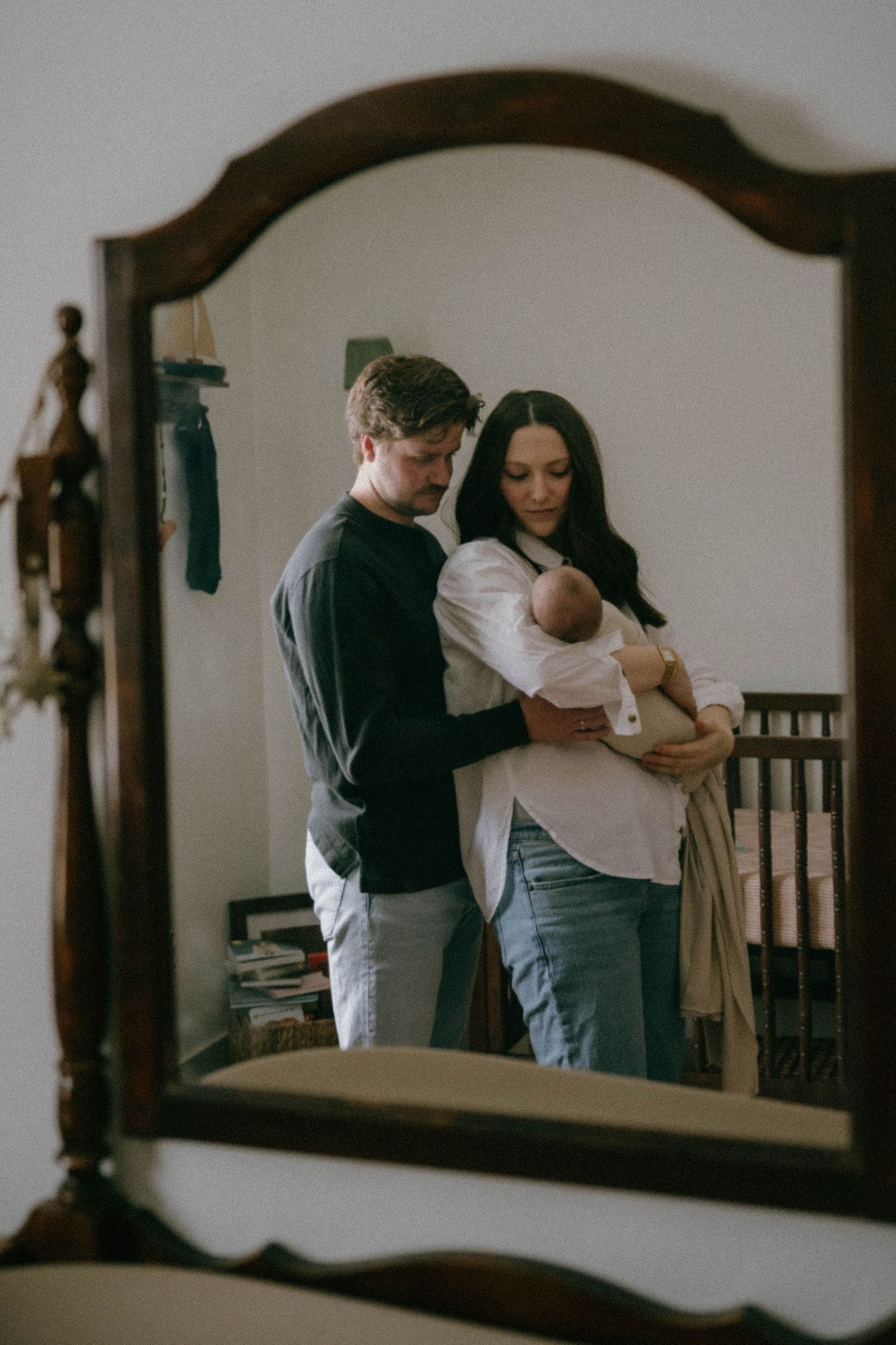 New parents admire their newborn baby together, reflected in a vintage mirror.