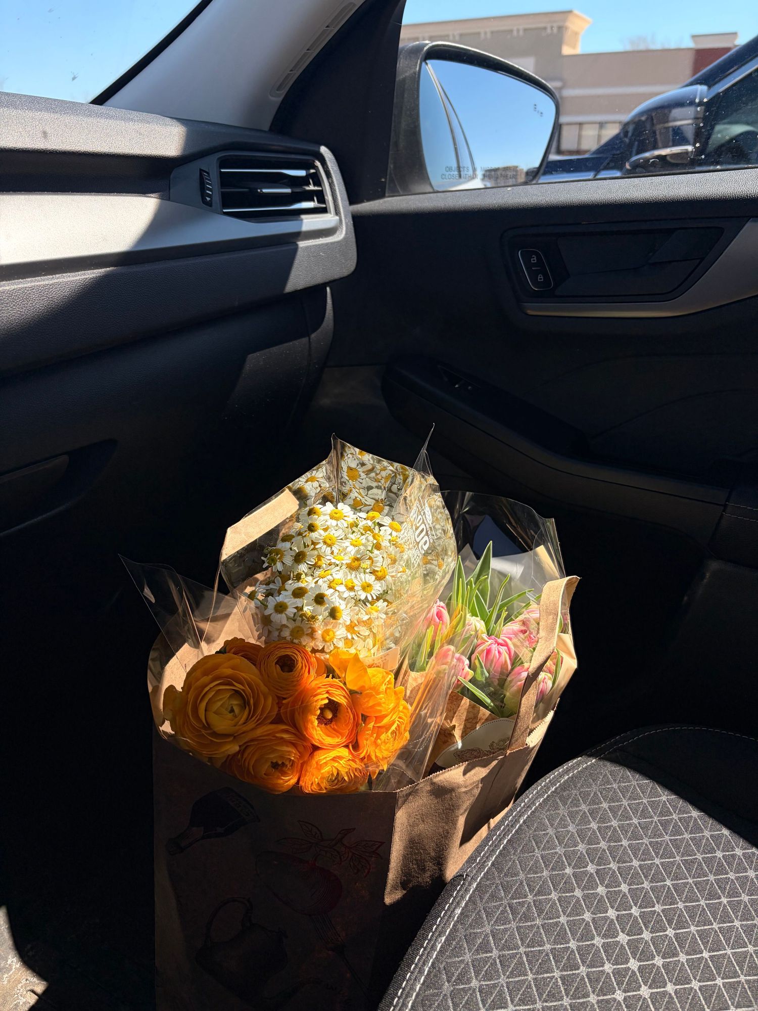 Fresh bouquet of orange ranunculus and white daisies sitting in car passenger seat on sunny day.