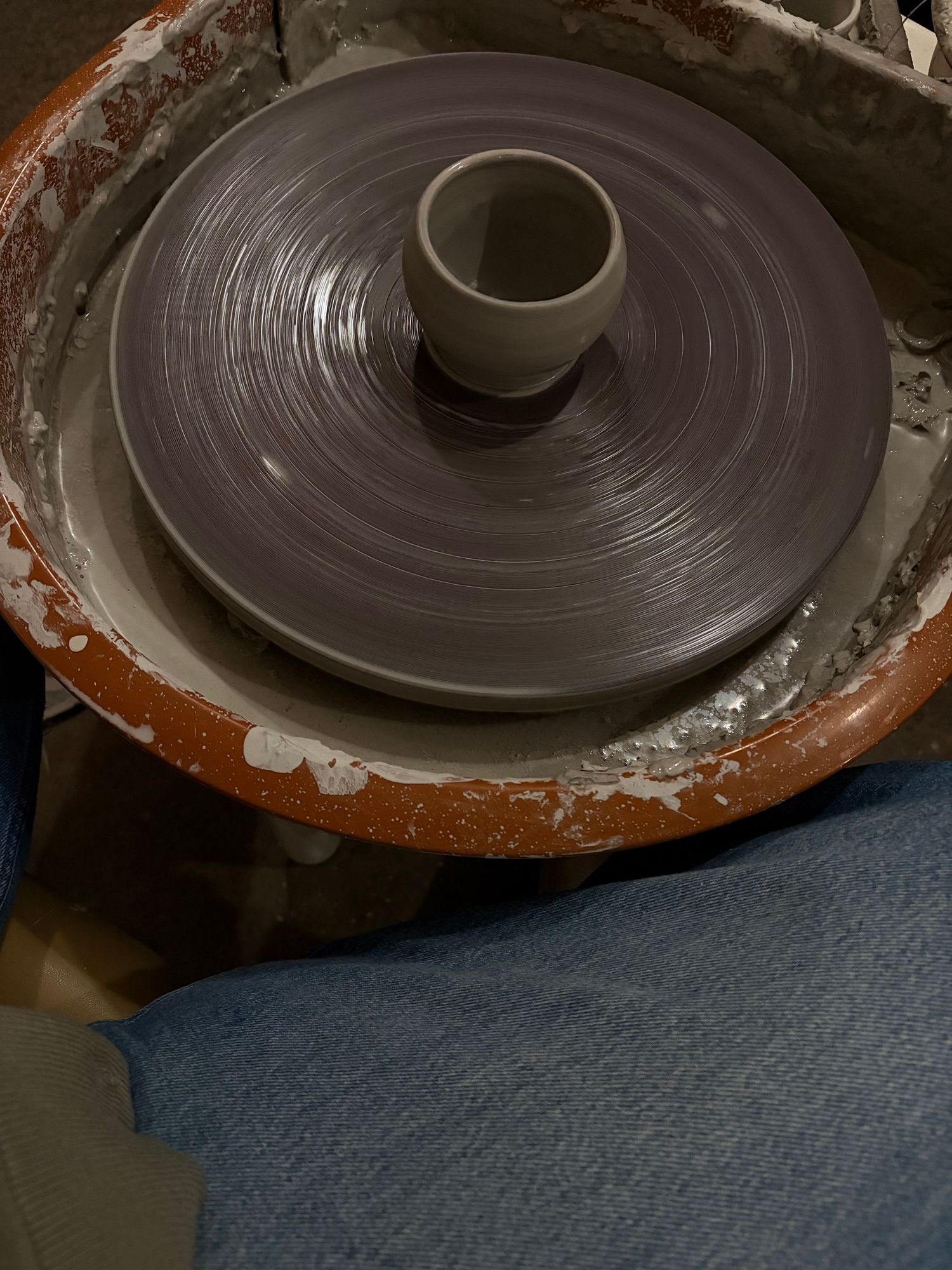 Gray clay being shaped on a pottery wheel with wet clay texture visible during ceramics class.