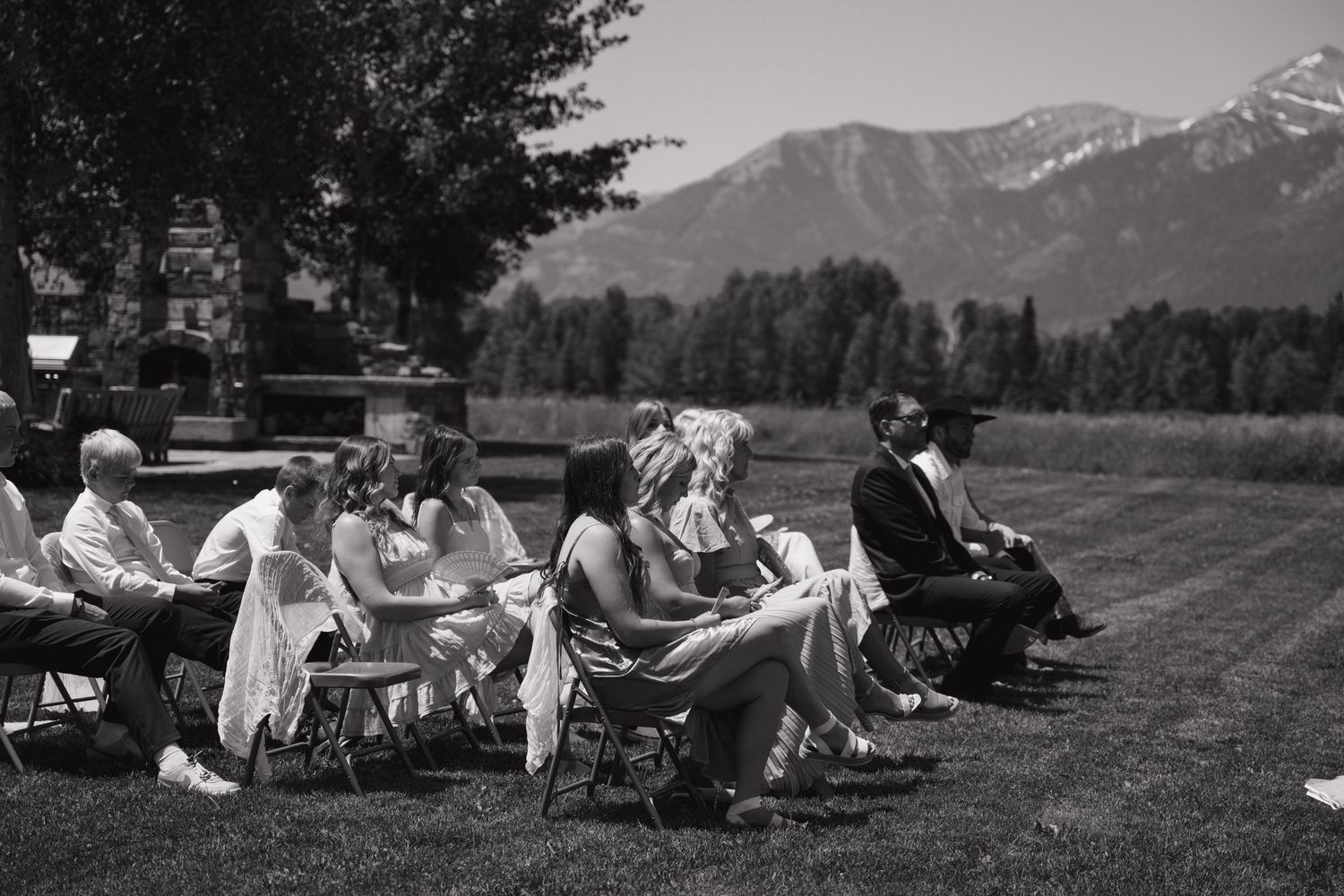 Black and white photo of wedding guests seated in chairs on lawn with mountain landscape in background.