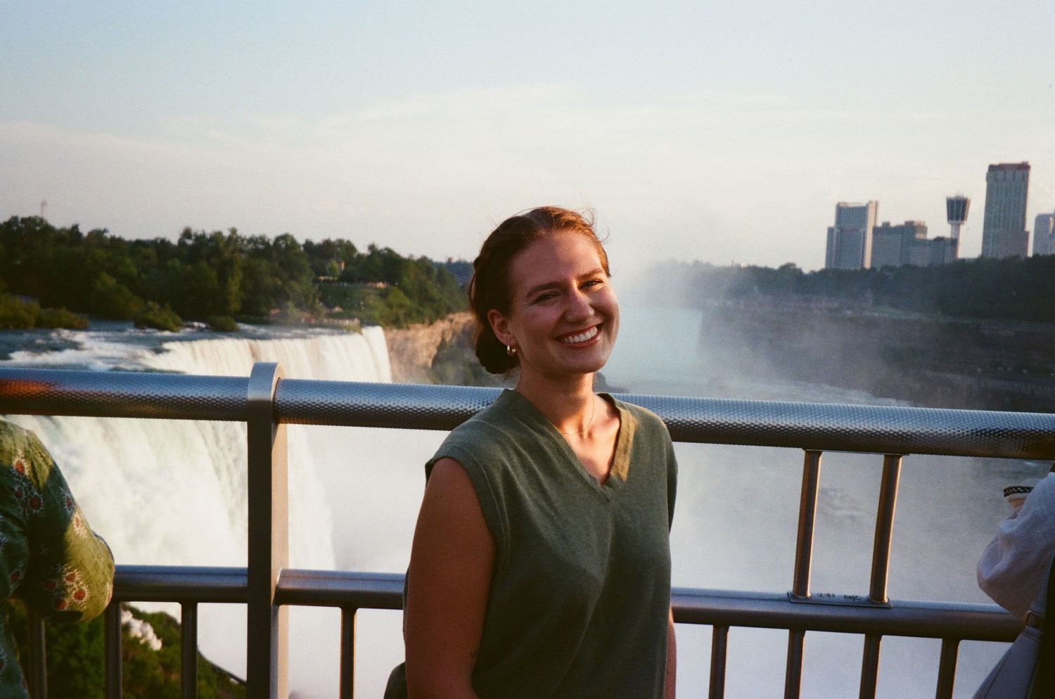 Smiling woman in green top laughing in front of Niagara Falls at golden hour on observation deck.