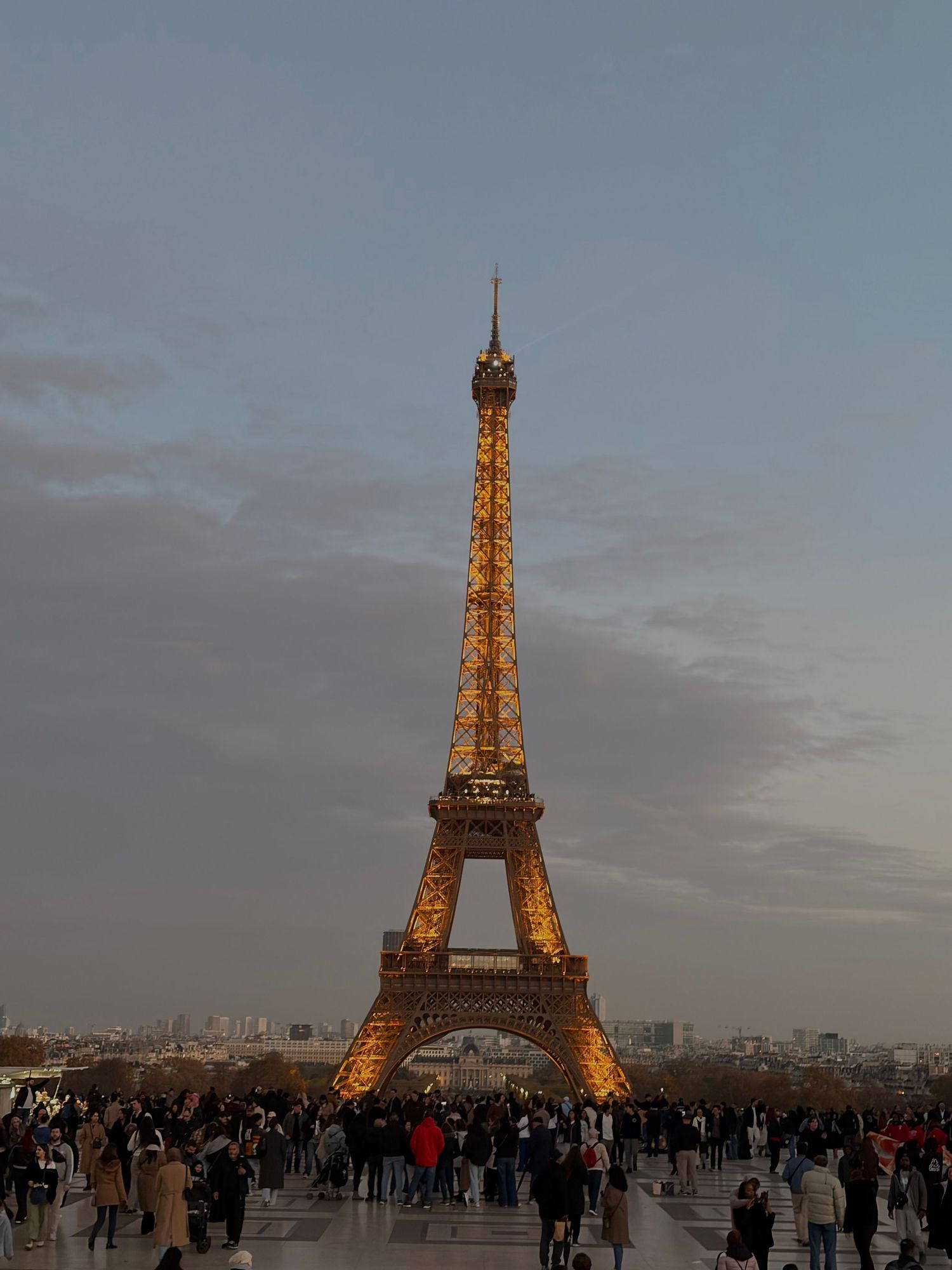 Illuminated Eiffel Tower glowing gold at dusk surrounded by crowds of tourists in Paris.